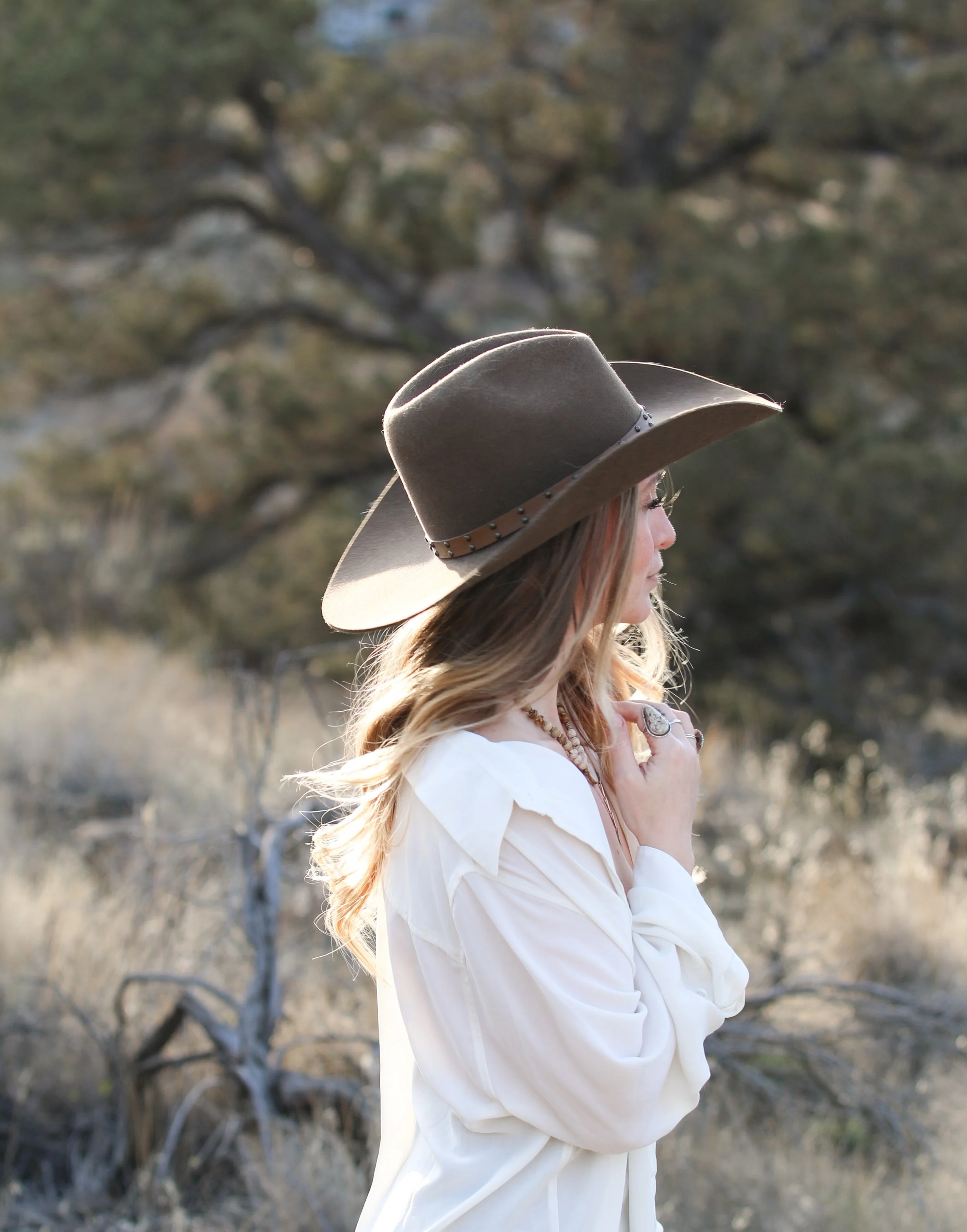 Western-inspired portrait of Dominique Noël photographed outdoors among Oregon juniper landscapes, reflecting her editorial storytelling style and American West aesthetic.