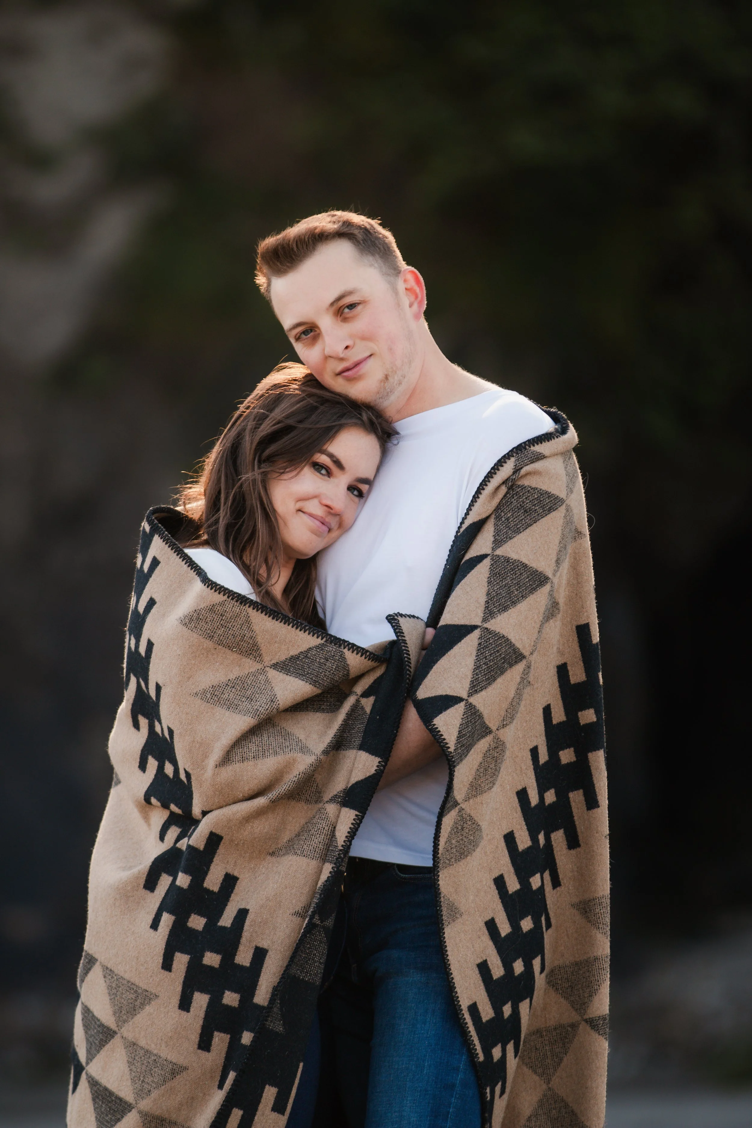 Couple embracing beneath dramatic coastal cliffs during an editorial engagement session. Oregon Coast.