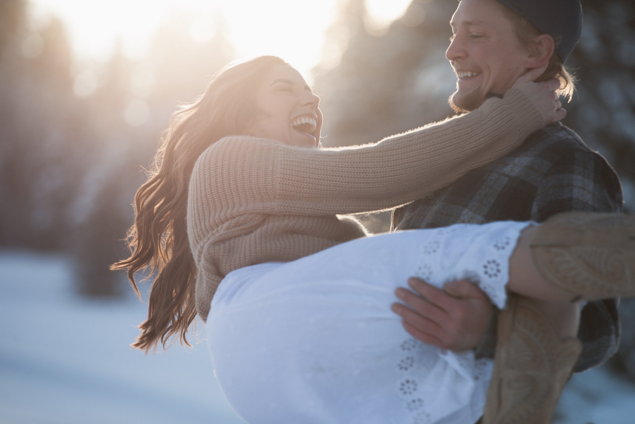 Engaged couple laughing as the groom lifts his bride-to-be in the snow near McCall, Idaho.