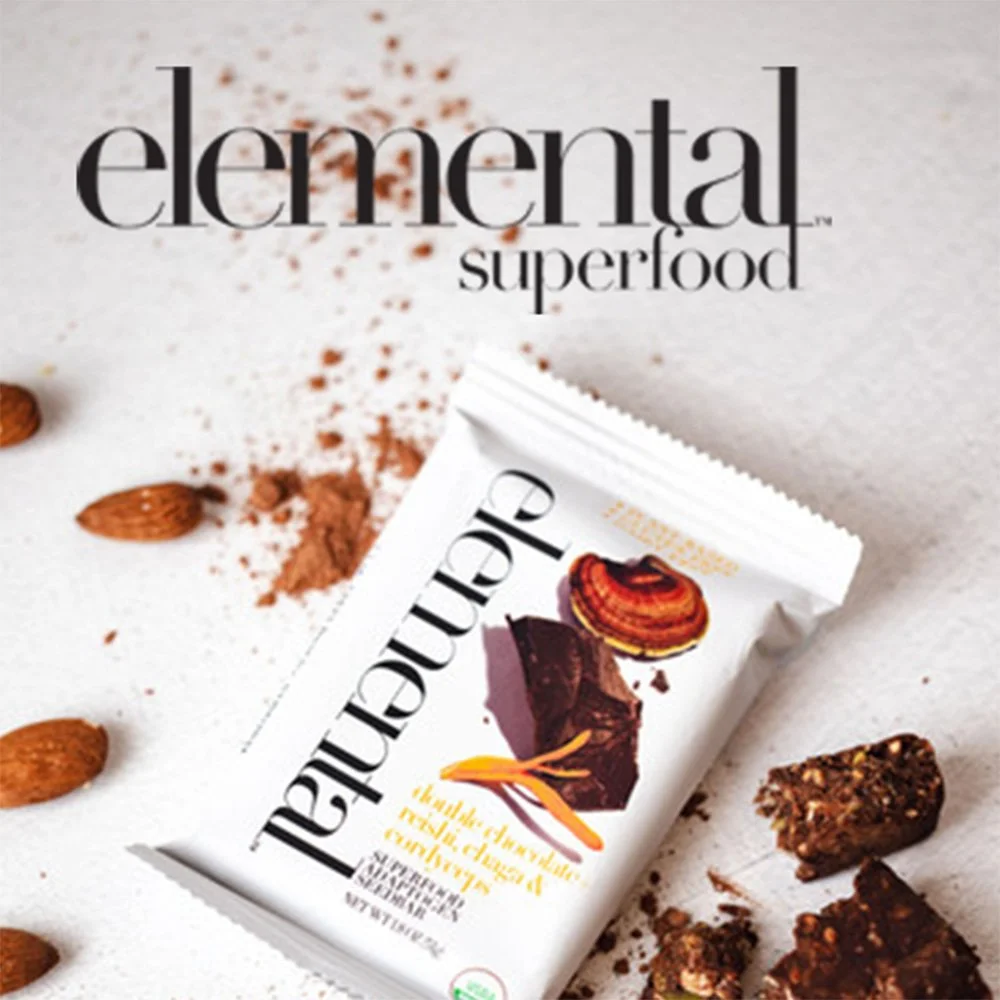 Packaging of a chocolate superfood snack bar with images of cacao, a vanilla bean, and an orange peel, surrounded by almonds, cacao powder, and chunks of the bar.