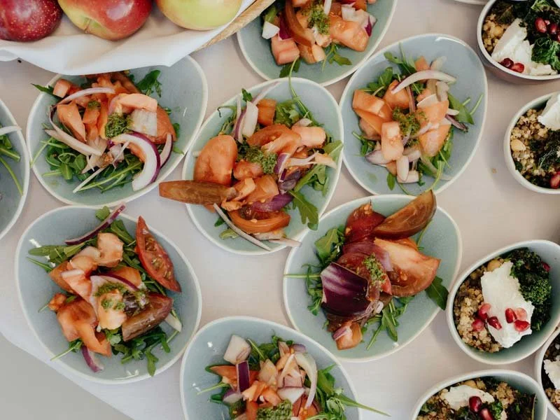 Multiple small bowls containing mixed salads with tomatoes, onions, leafy greens, and dressings, arranged on a light-colored table.