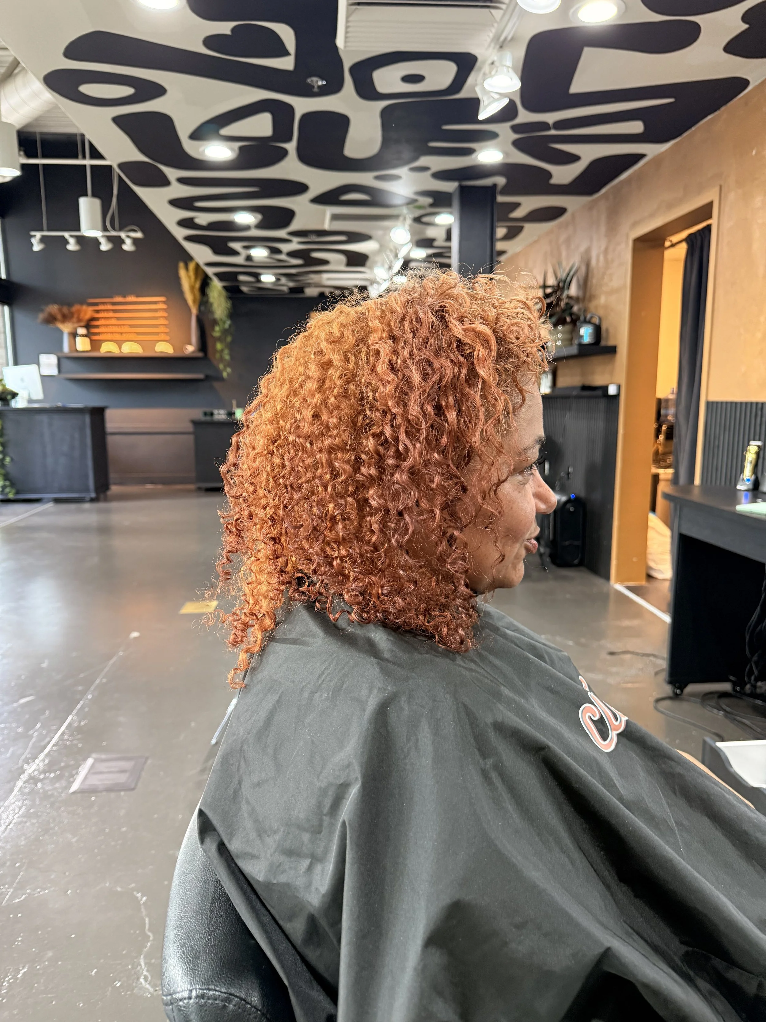 A woman with curly, reddish-orange hair sitting in a hair salon.