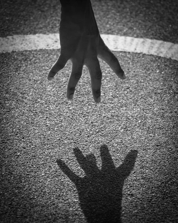 A hand reaching downward over a textured surface, casting a shadow of the hand on the ground.