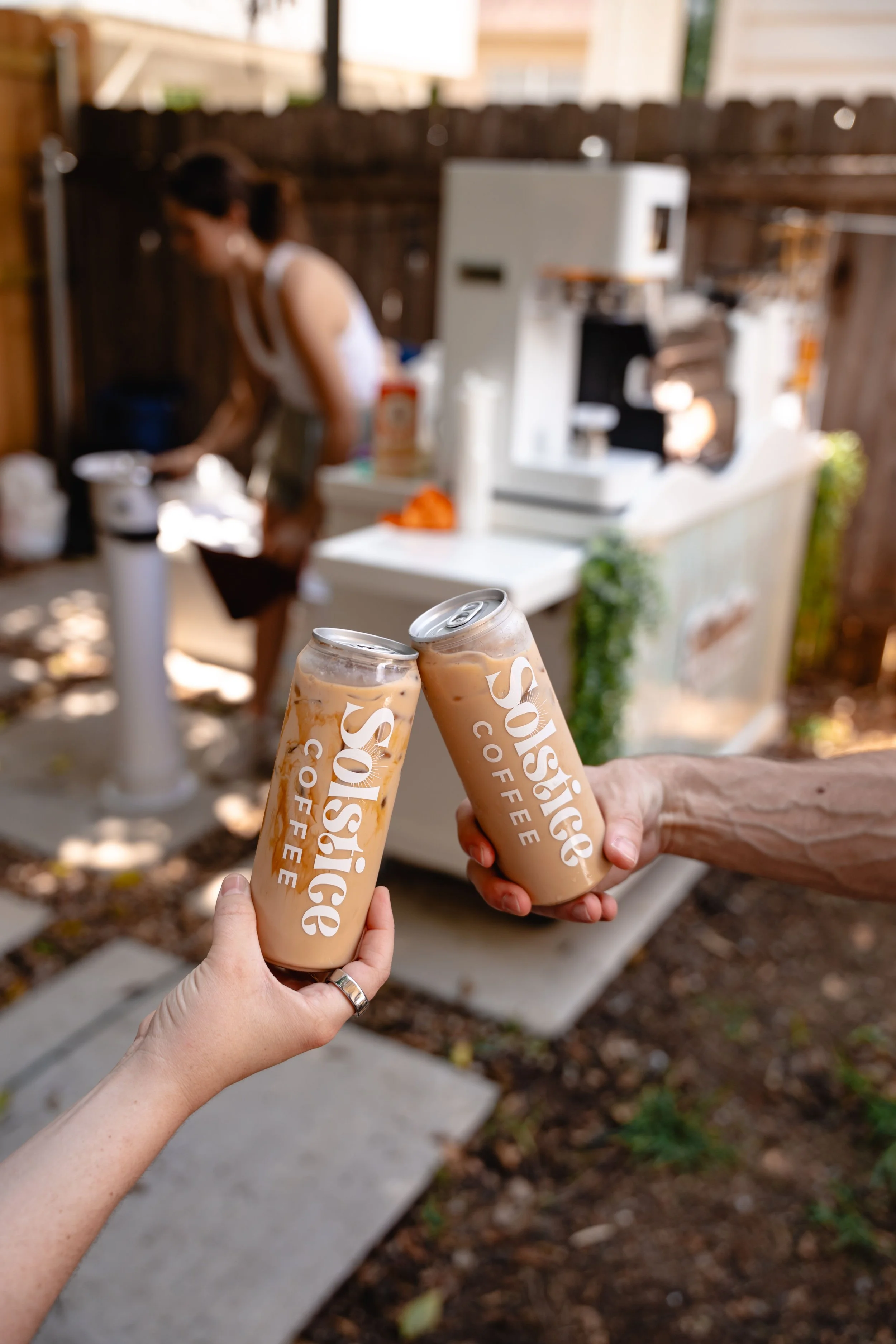 Two people holding custom canned lattes from solstice coffee cart at a private event with coffee catering in austin texas.