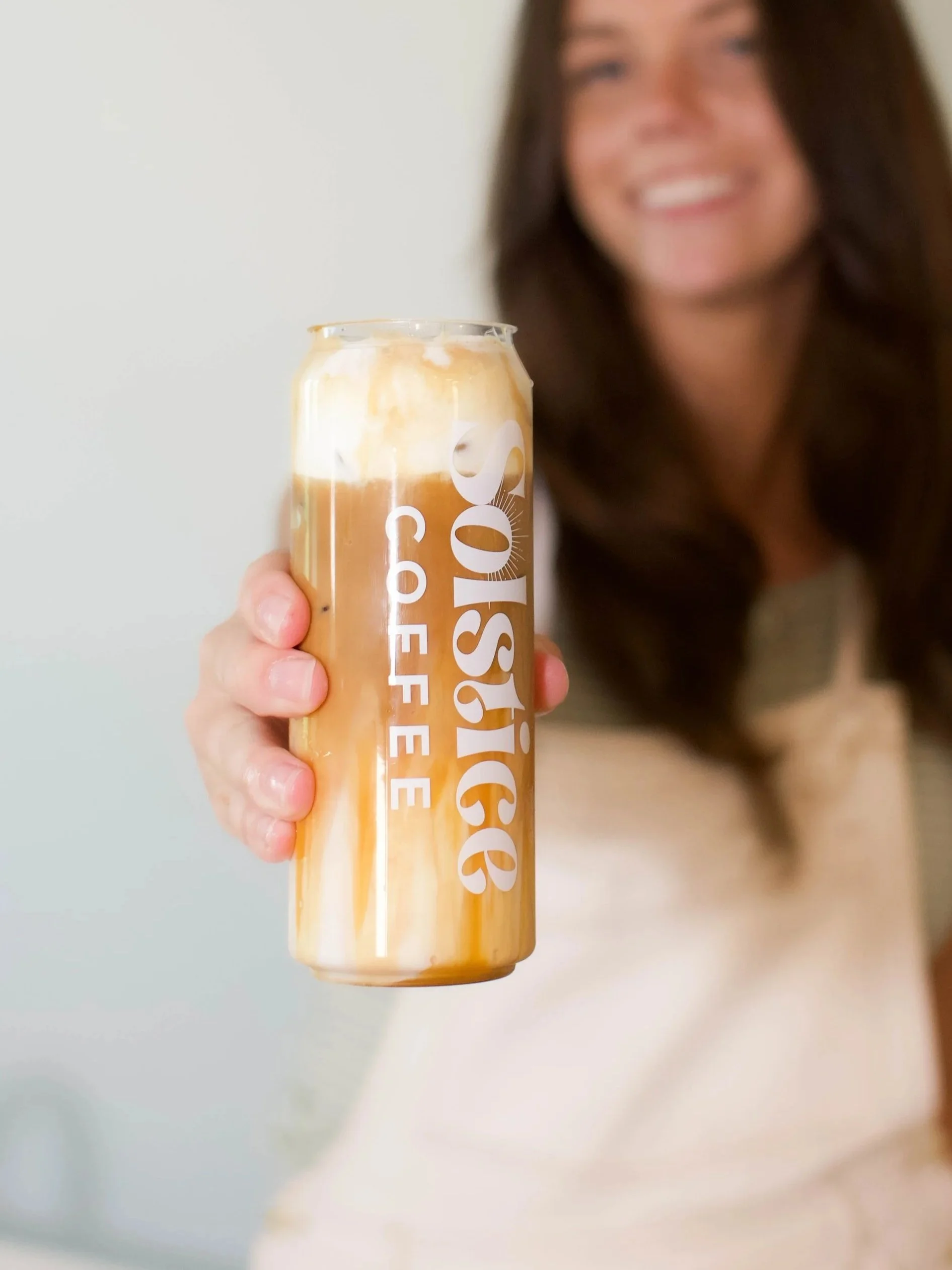 Shows a canned latte being held by a girl towards the camera to show the espresso drink with cold foam from her coffee cart.