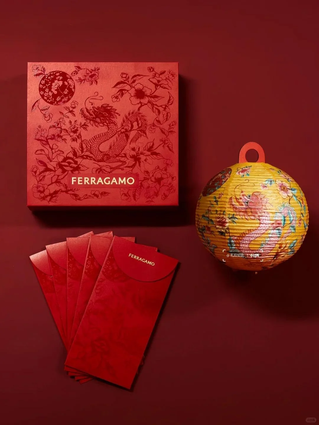 A red Ferragamo box with a dragon and floral design, five red envelopes with the Ferragamo logo, and a yellow paper lantern with a dragon illustration, all set against a red background.
