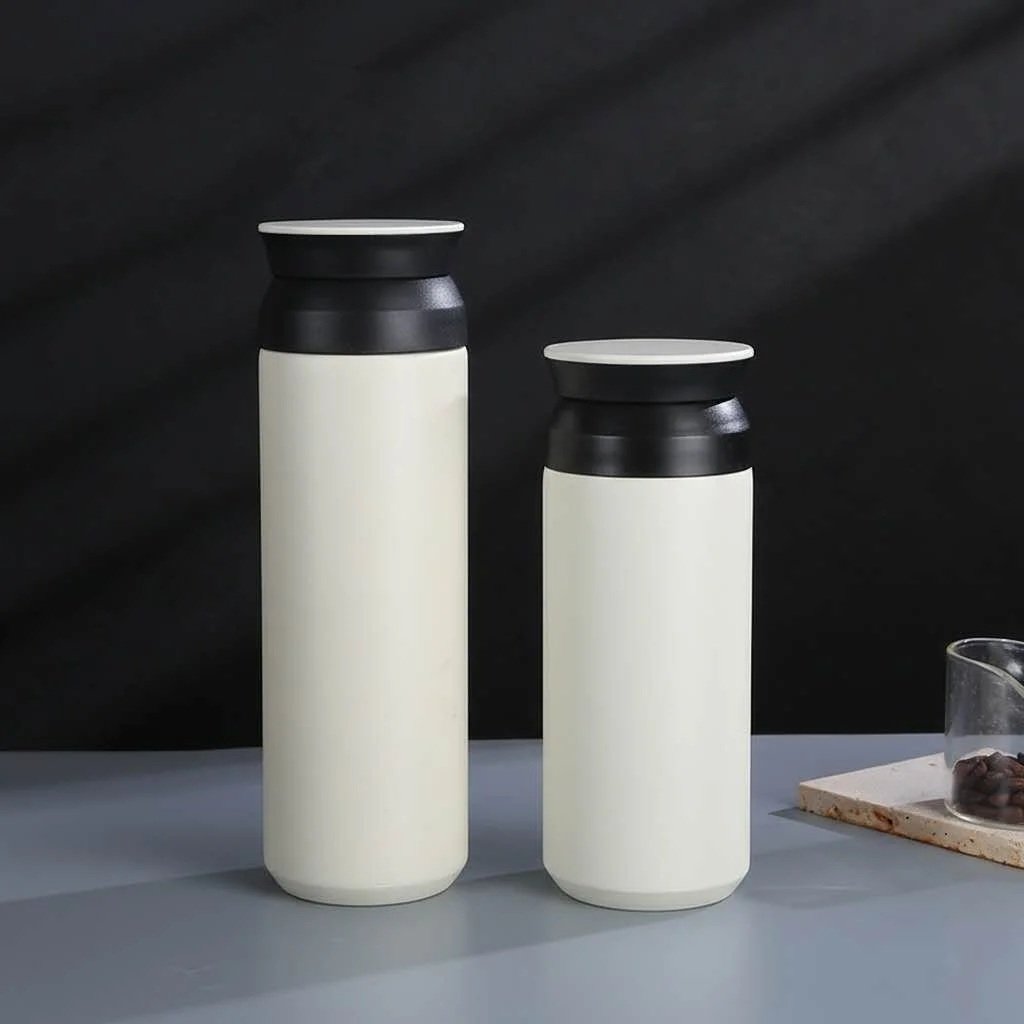 Two sleek, modern thermos bottles with white bodies and black lids are positioned on a gray surface against a dark background.