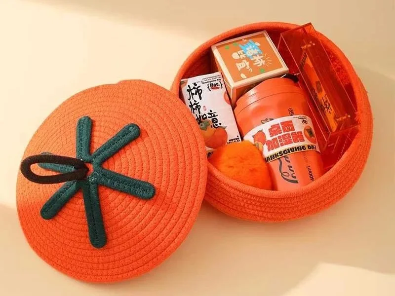 An orange circular container with a lid, filled with various small items including packets, a cup, and a fluffy orange object, all placed on a white surface.