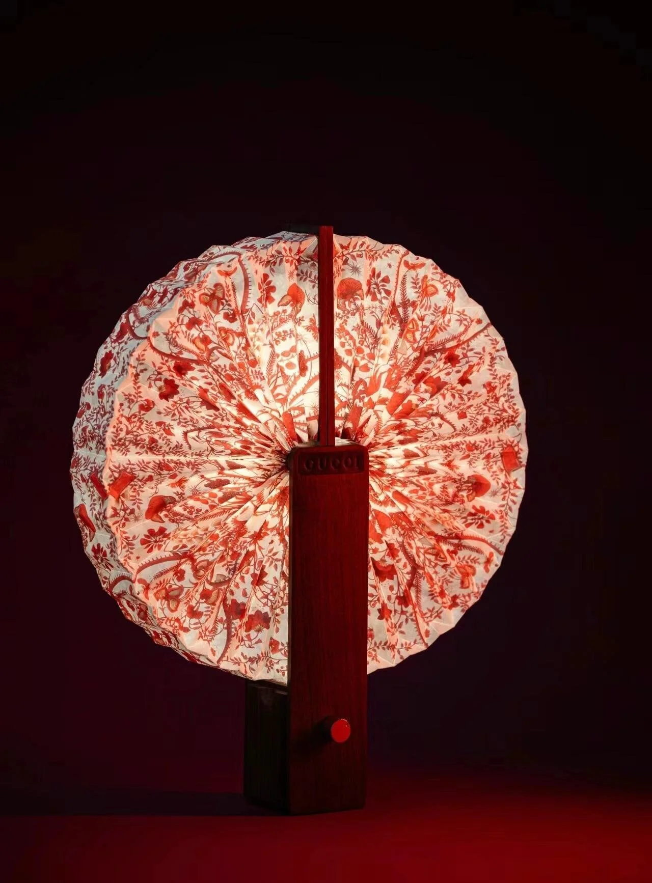 Red and white patterned paper lantern with a wooden handle, illuminated against a dark background.