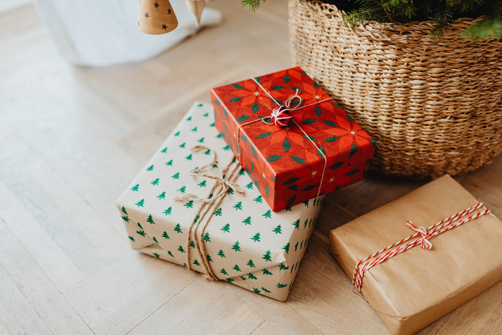 Three wrapped Christmas presents under a decorated tree, with a woven basket nearby.