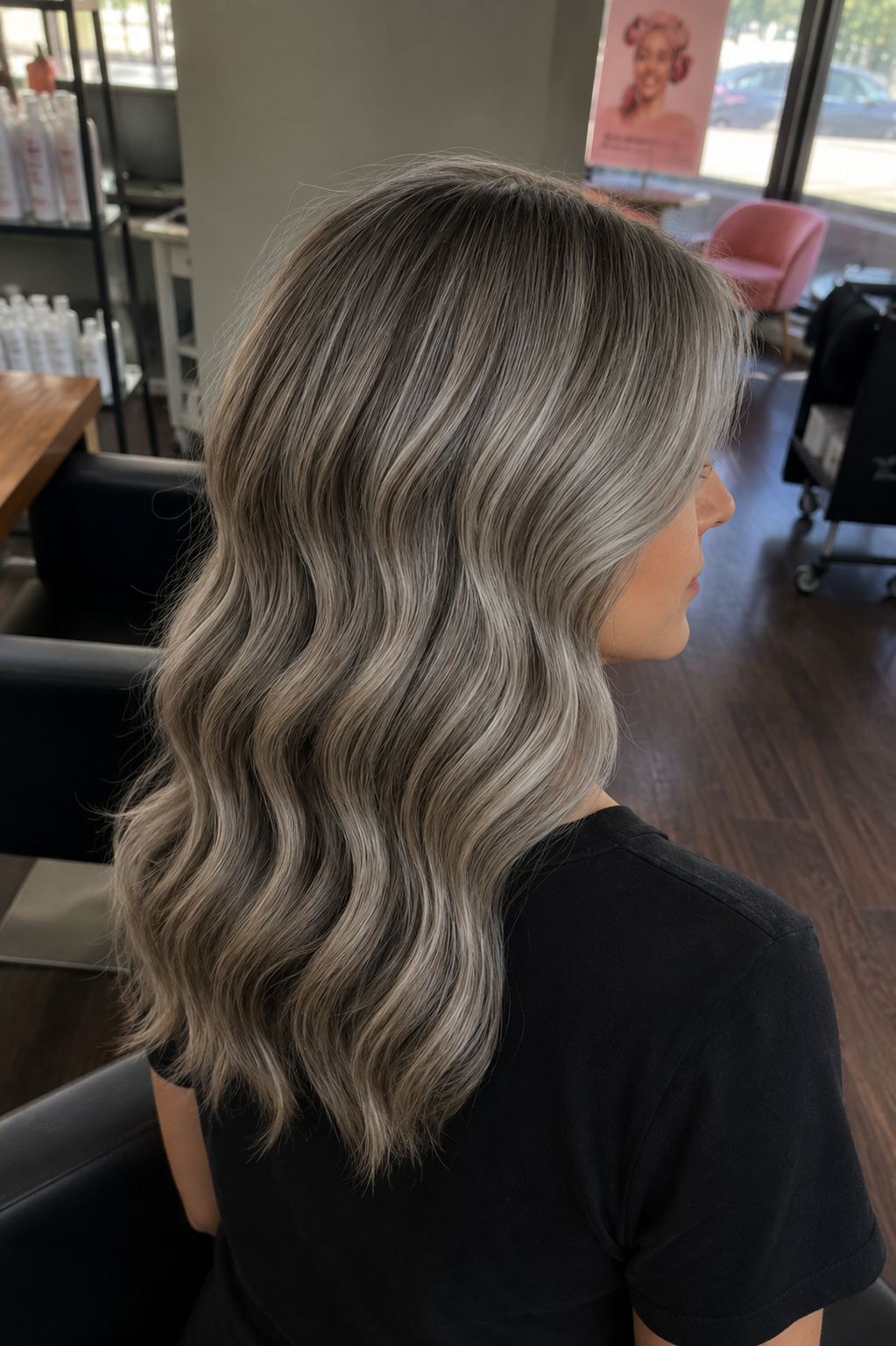 A woman with shoulder-length wavy gray hair sitting in a salon and facing sideways.