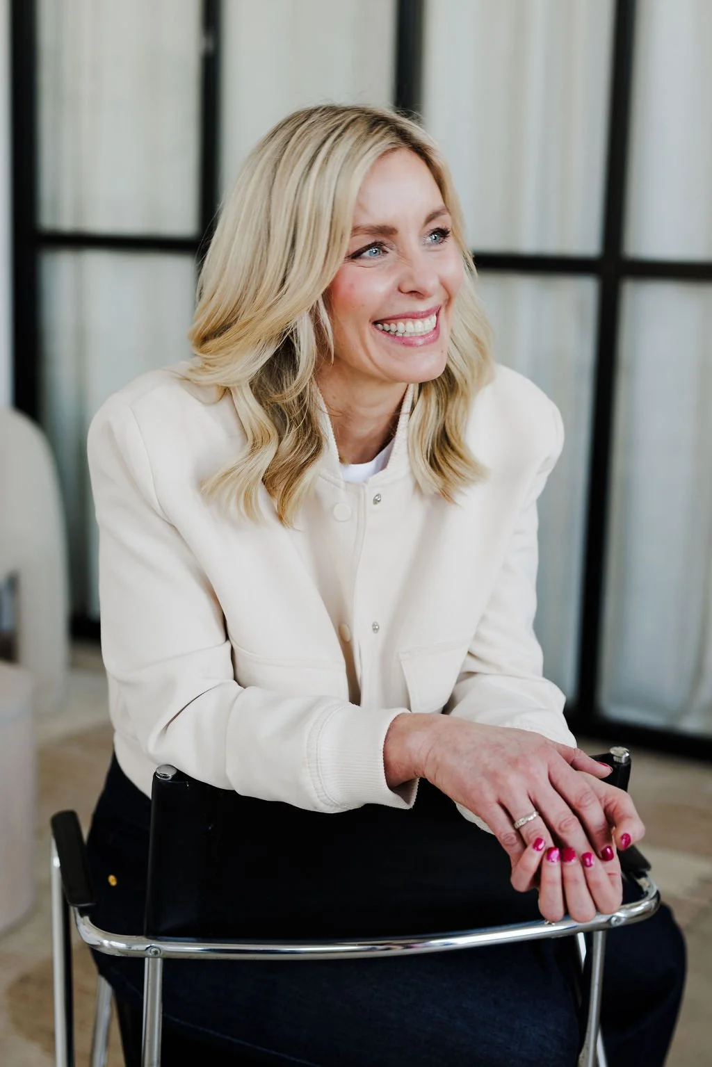 A smiling woman with blonde hair sitting on a wheelchair in an indoor setting.