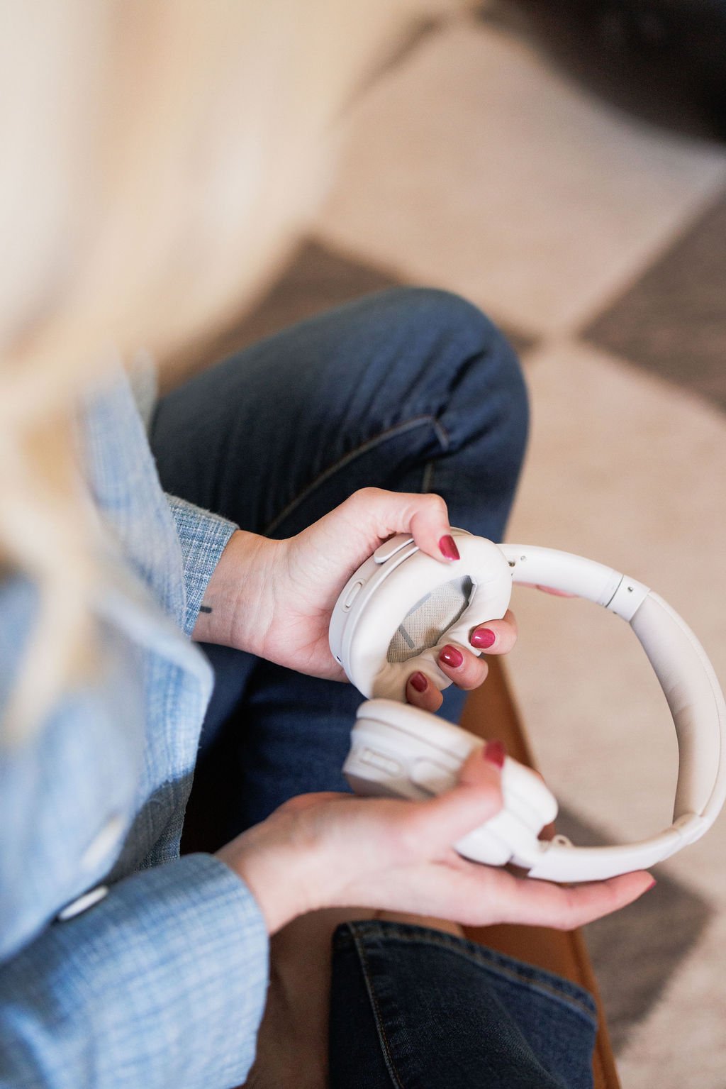 A person holding a pair of white over-ear headphones with both hands, sitting on a wooden chair.