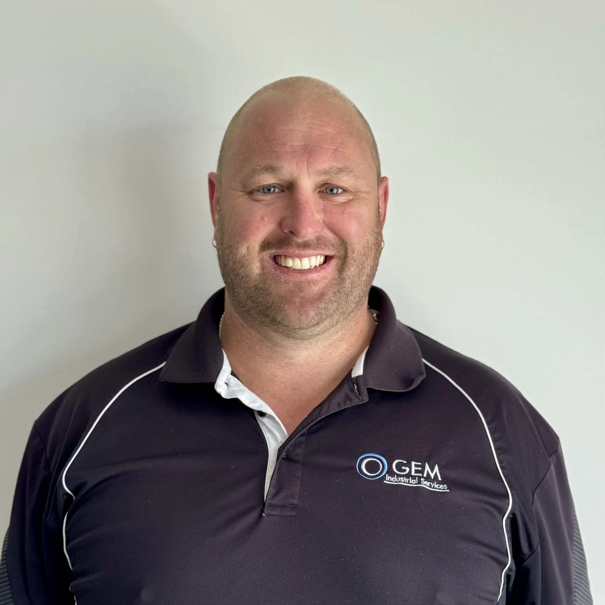 Smiling man with a beard and short hair wearing a black polo shirt with the logo of GEM Industrial Services.