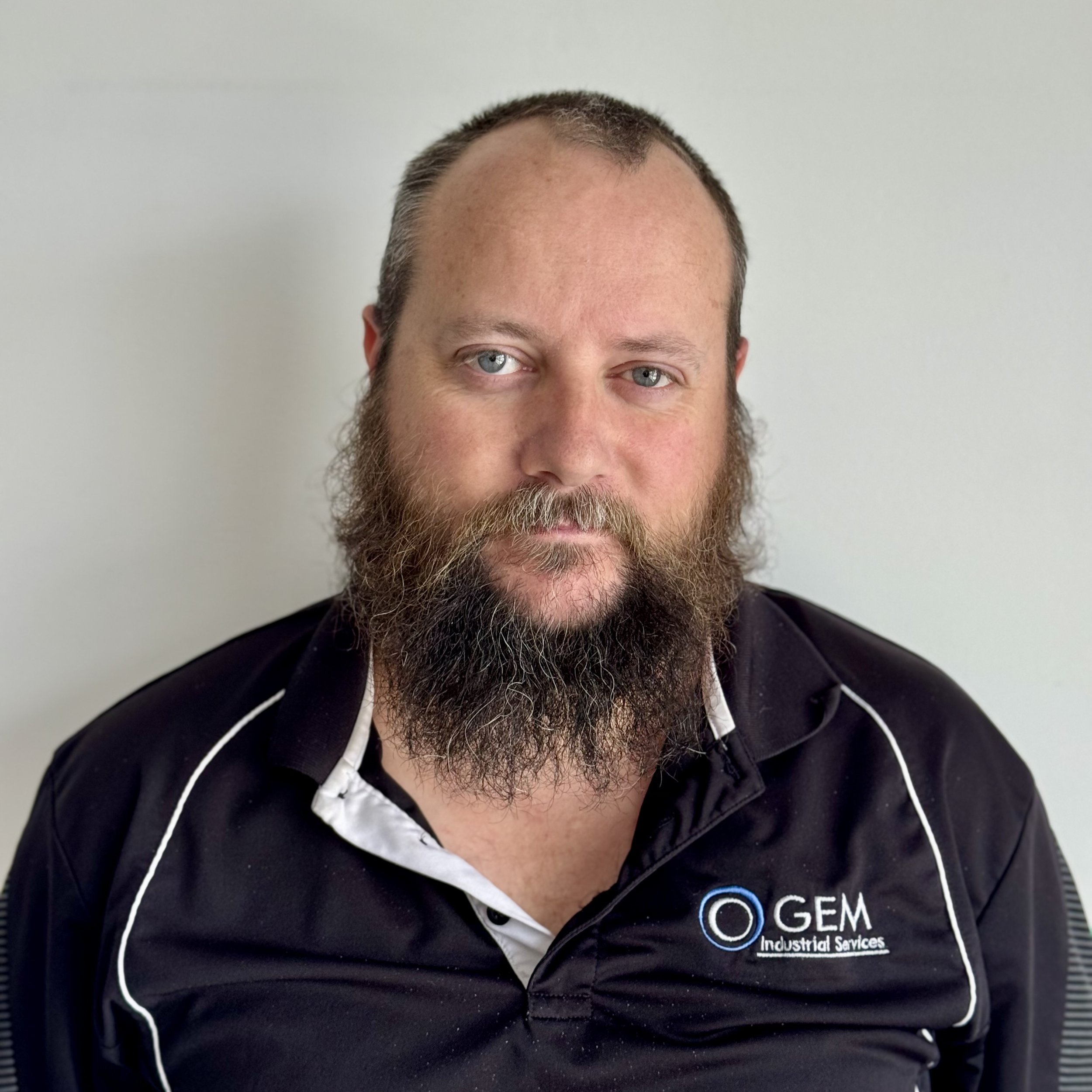 A man with a beard and short hair wearing a black polo shirt with the logo and name 'GEM Industrial Services'.