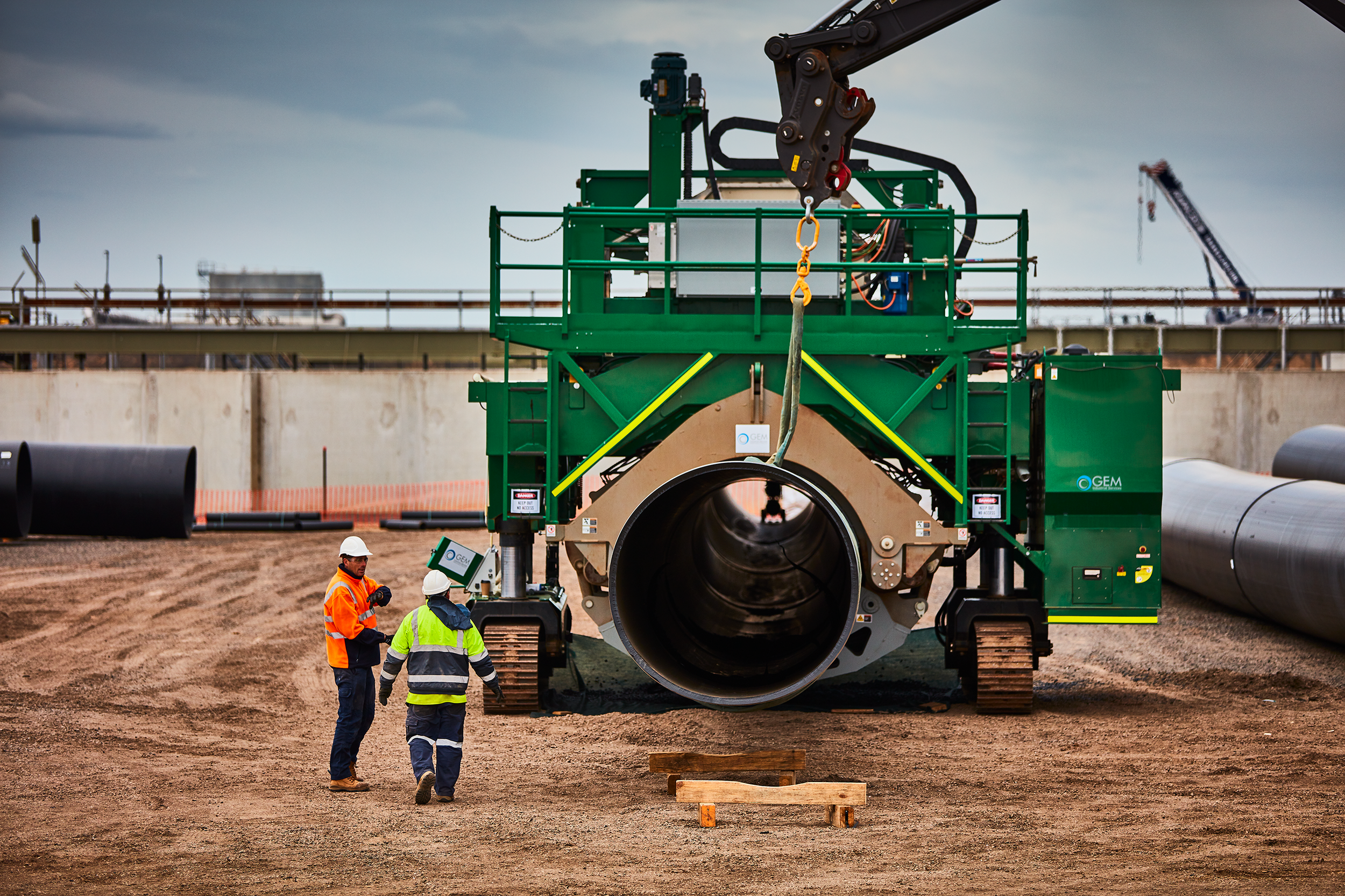 Construction workers in safety gear working near large industrial pipe installation at construction site.