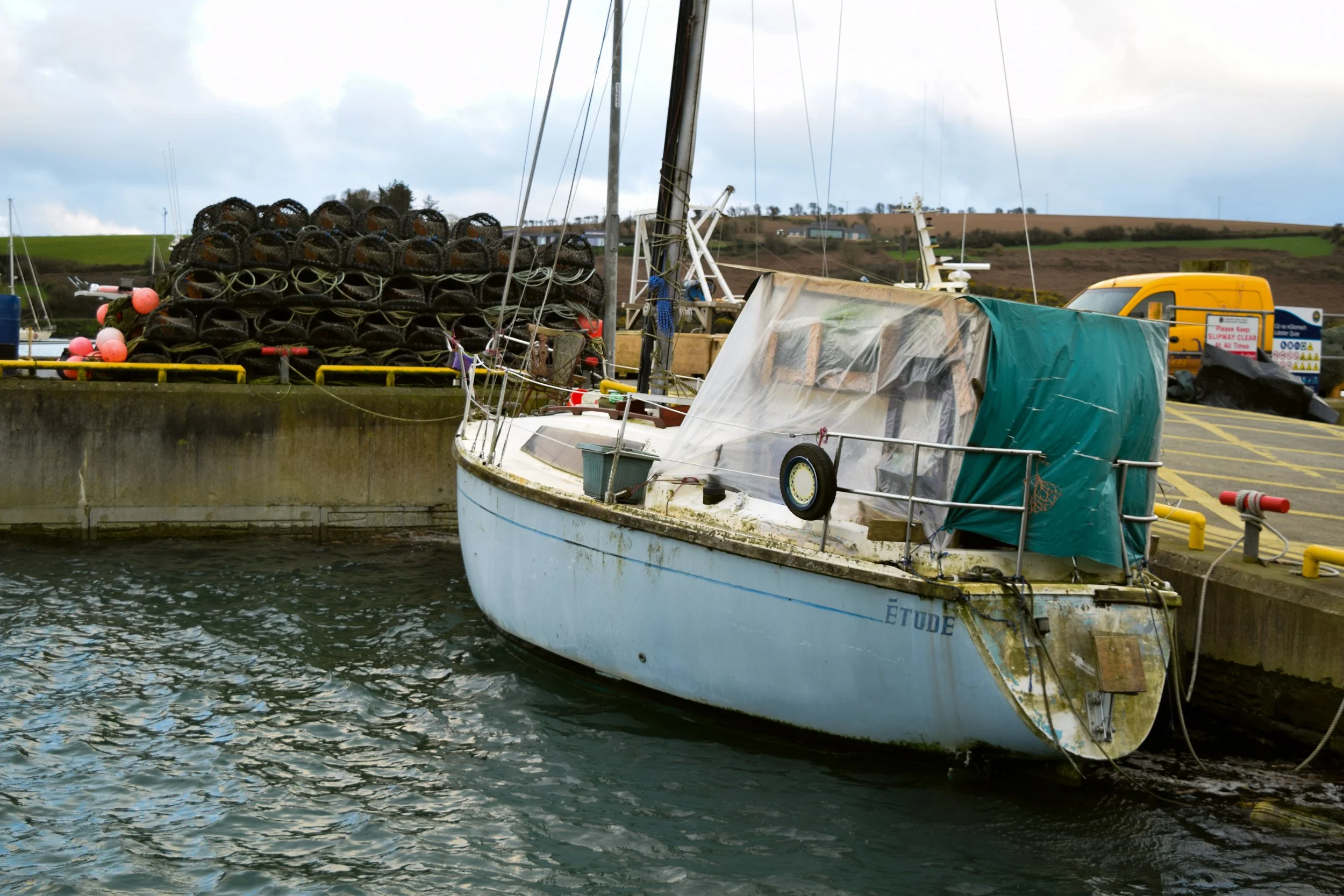 A sailboat docked at a harbor with stacked tires and buoys in the background.