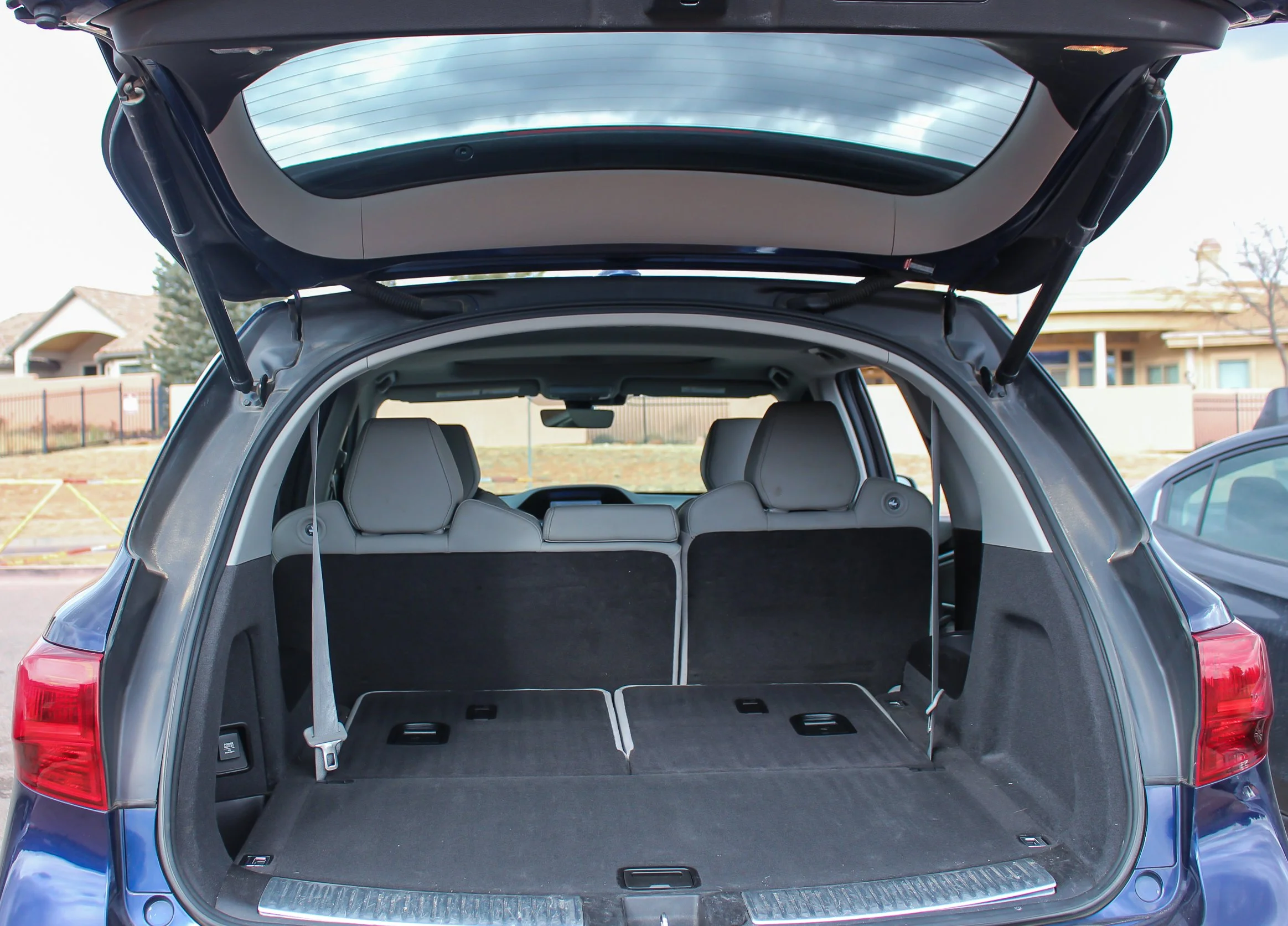Open trunk of a modern SUV with rear seats and a large cargo space in a residential area.