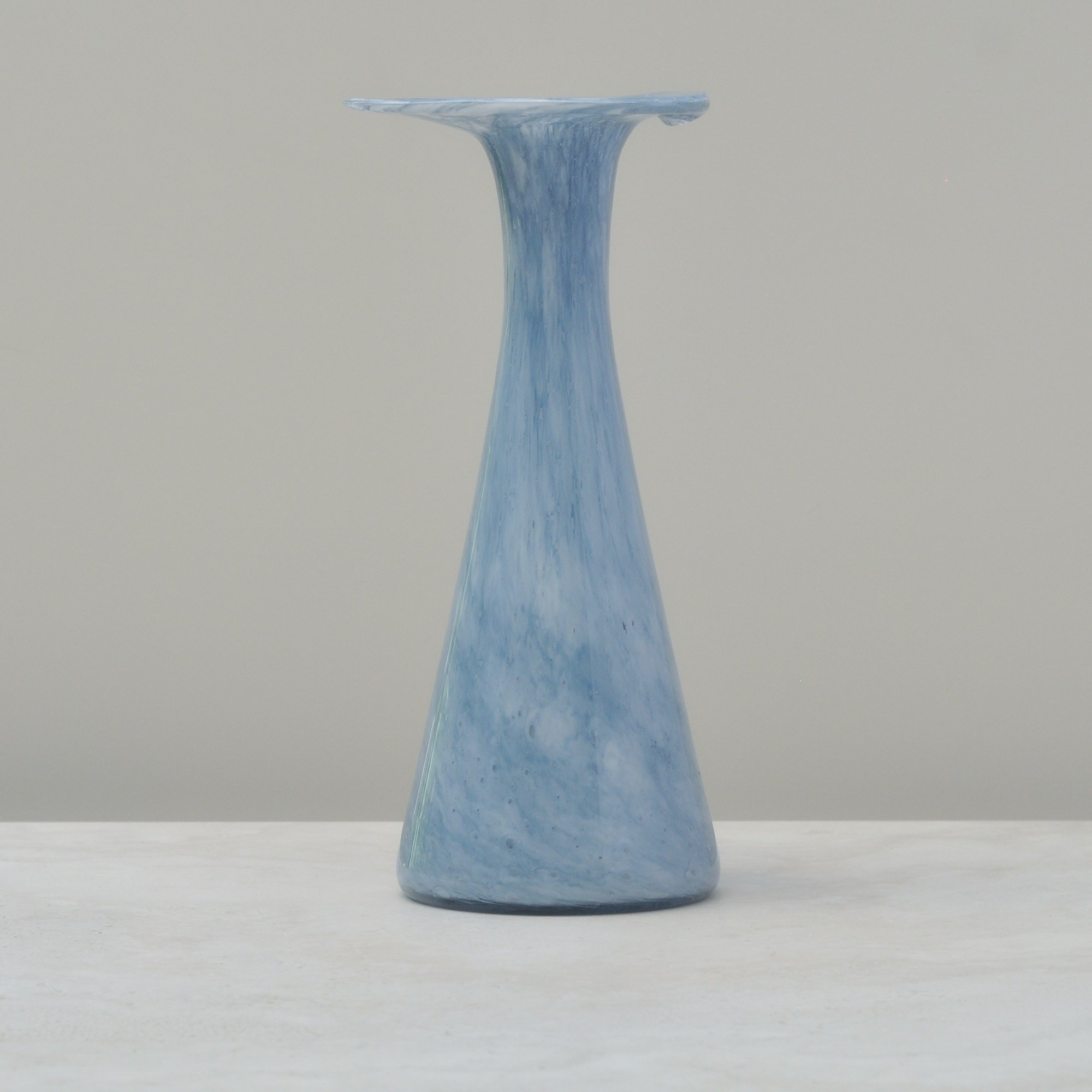 Front view of a light blue handblown glass vase with a soft marbled pattern and flared lip.