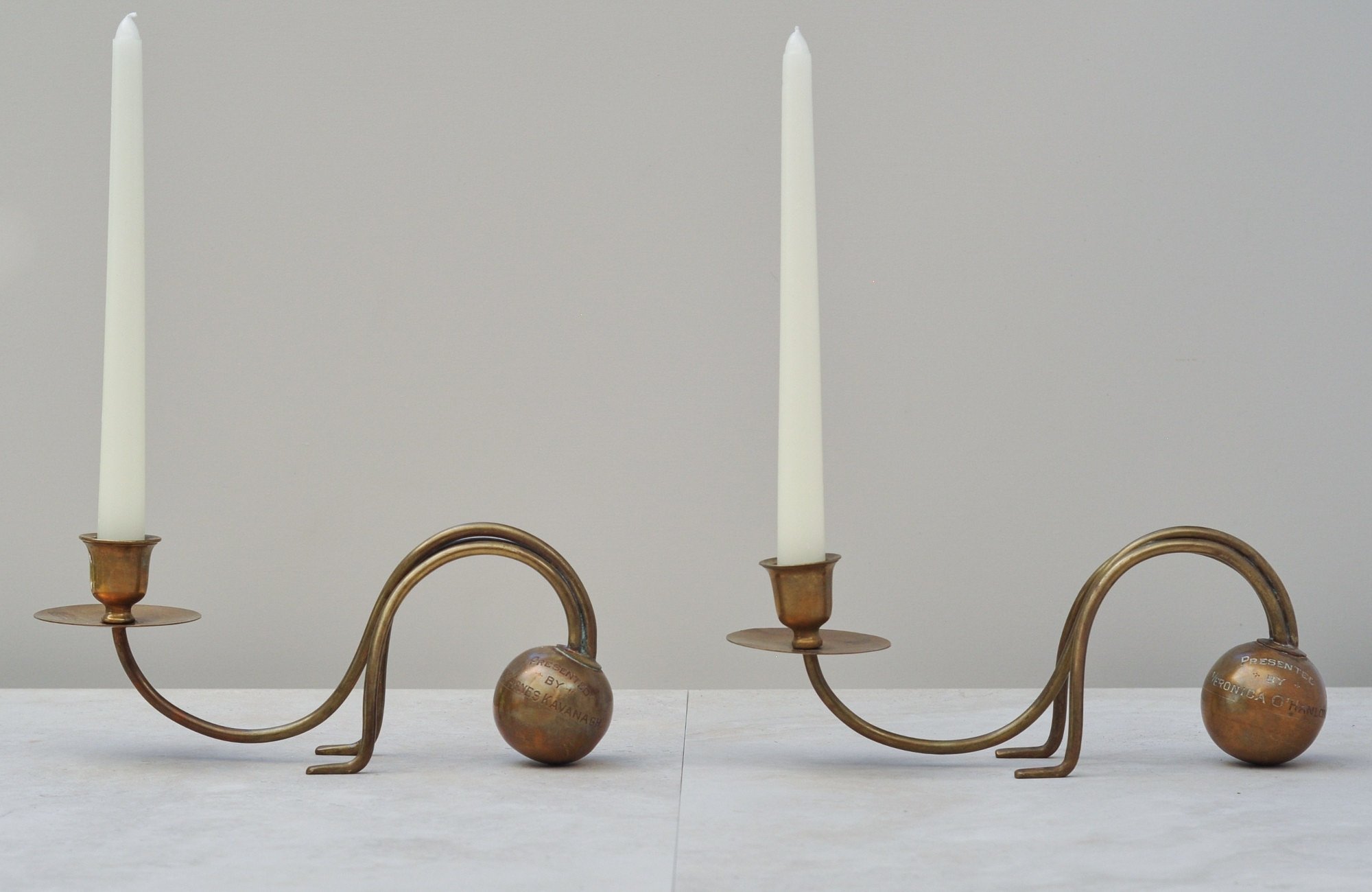 Pair of Presented By brass candleholders holding white taper candles.”