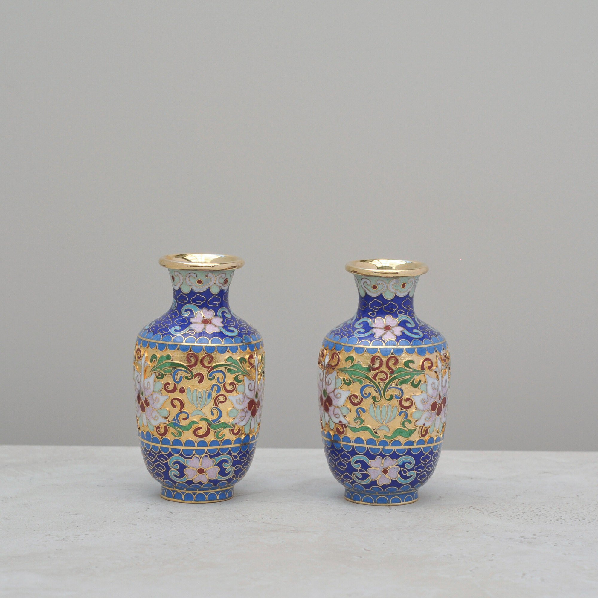 Pair of mid-century Cloisonné vases with colourful enamel floral designs and brass detailing, shown side-by-side on a neutral background.