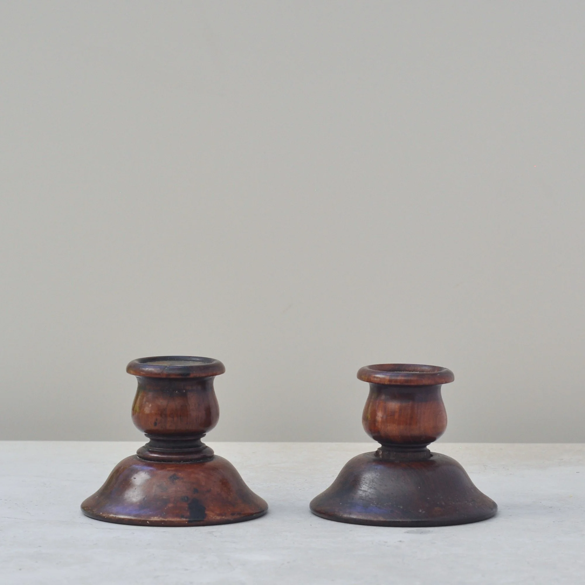 Side angle of antique turned wood candlesticks showing patina and rounded turned bases.