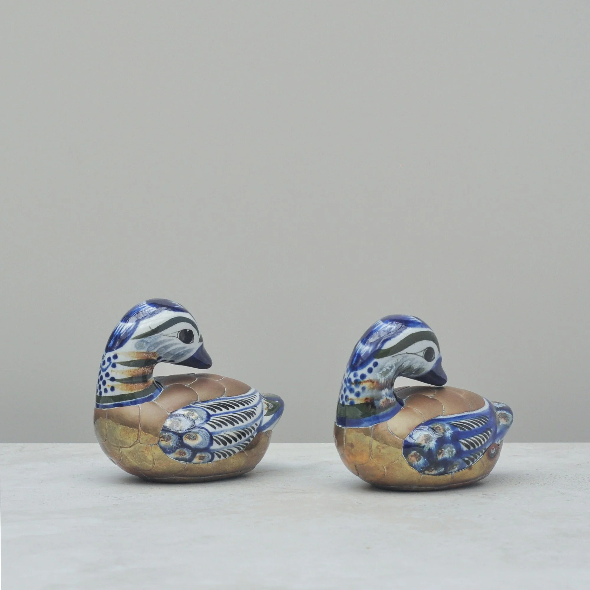 Pair of vintage Mexican Tonalá ceramic ducks with brass accents, shown side-by-side against a soft neutral background.