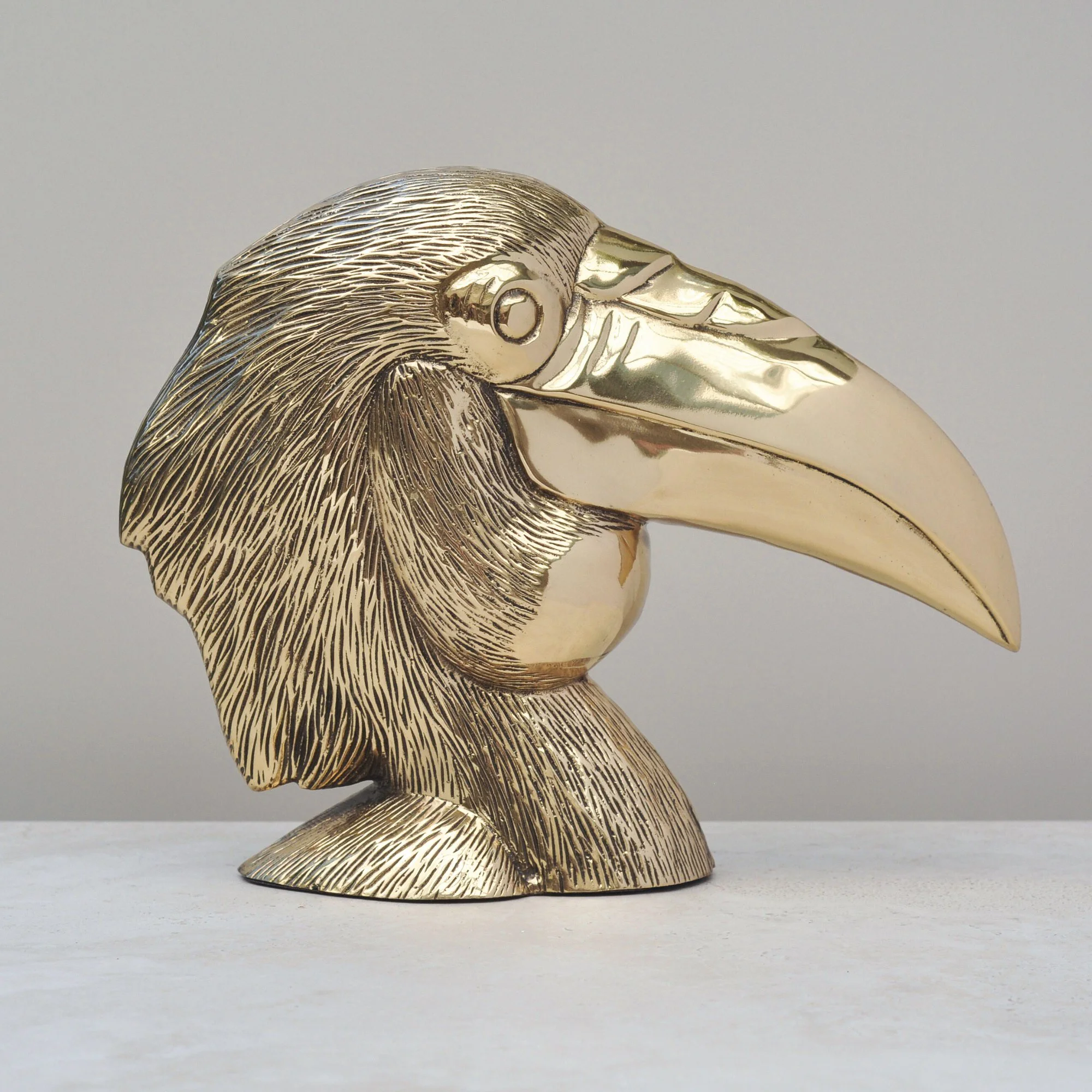 Brass bird head ornament with sculpted plumage and curved profile, side view