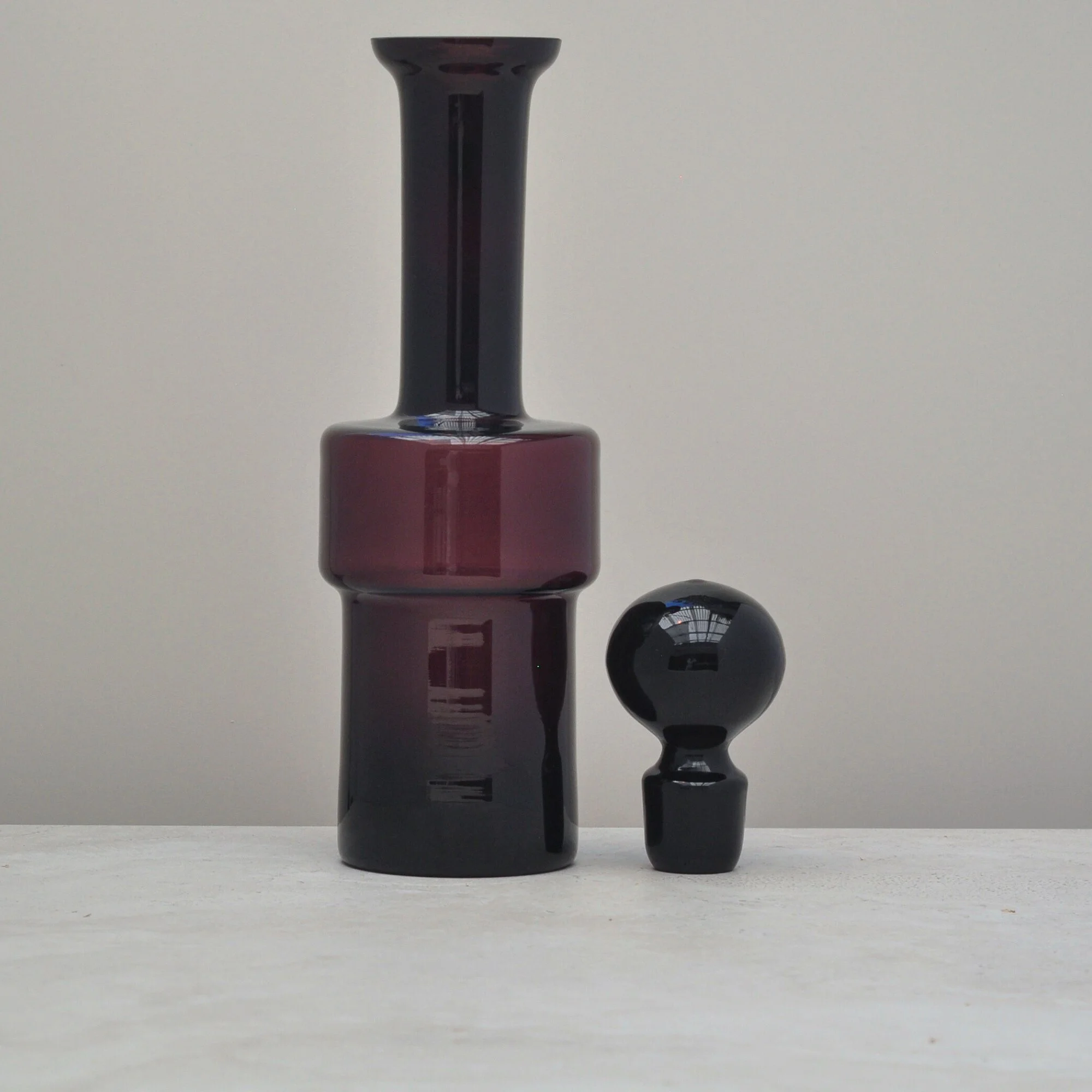 “Mid-century aubergine glass decanter displayed with its matching spherical stopper set beside it.”