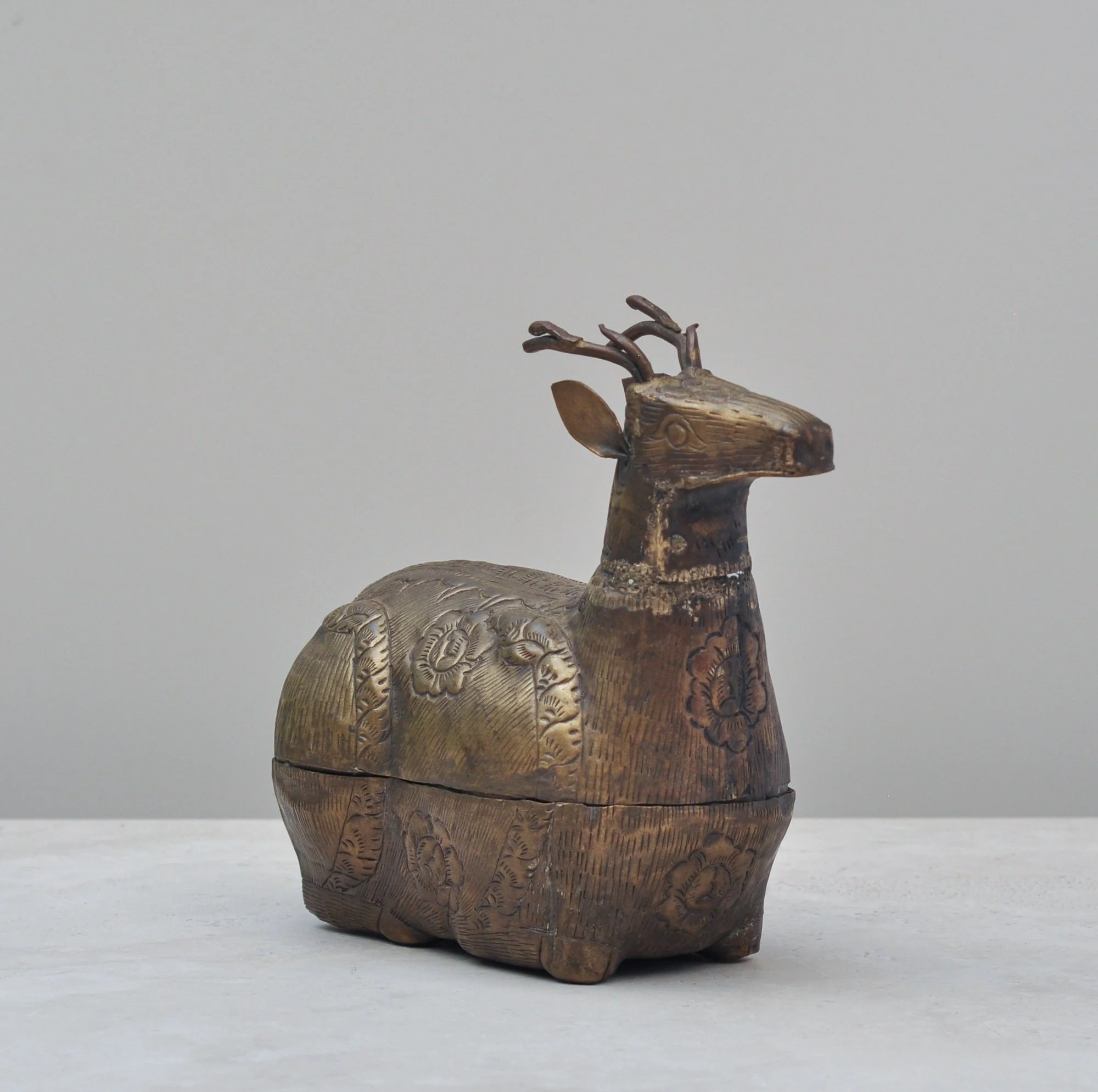 Side view of a vintage brass deer-shaped lidded box featuring engraved floral and geometric patterns.