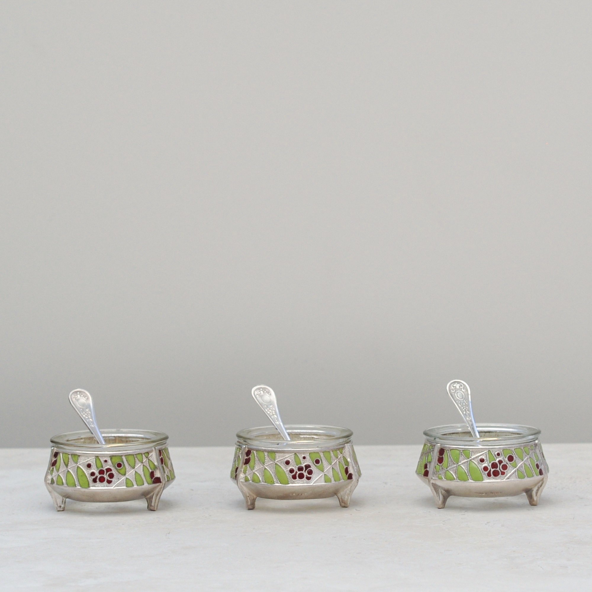 Set of three mid-century silver-plated salt cellars with cloisonné enamel and matching spoons, front view.