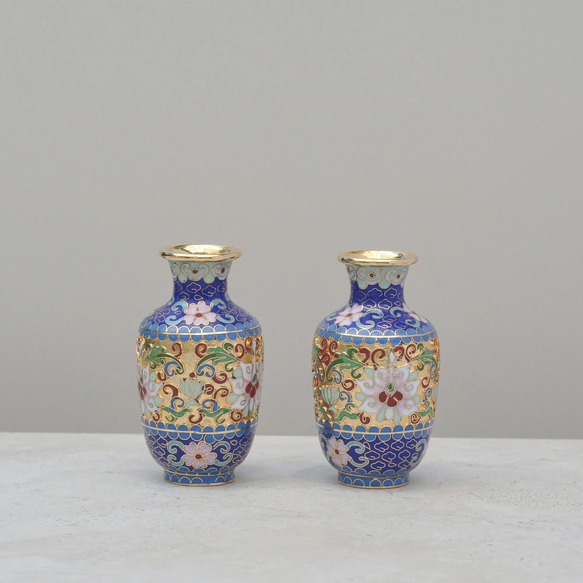 Front-facing view of a decorative Cloisonné vase pair showcasing vibrant enamel work in blue, pink, green and gold on brass.