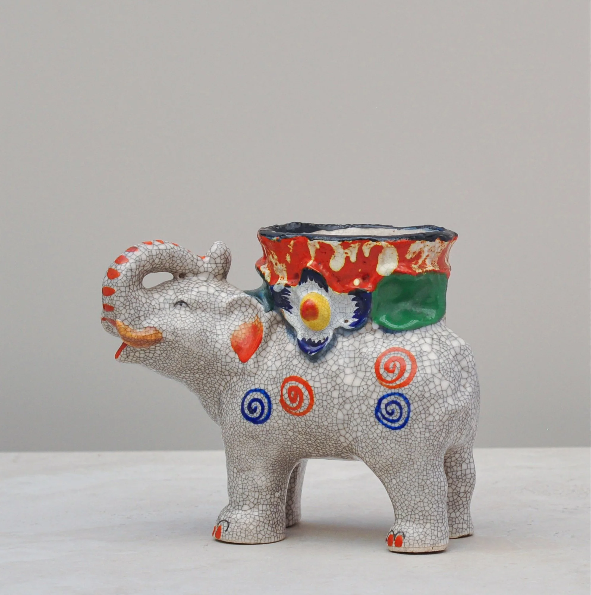 Crackle-glazed ceramic elephant vessel shown from the left side, featuring vibrant hand-painted decoration.