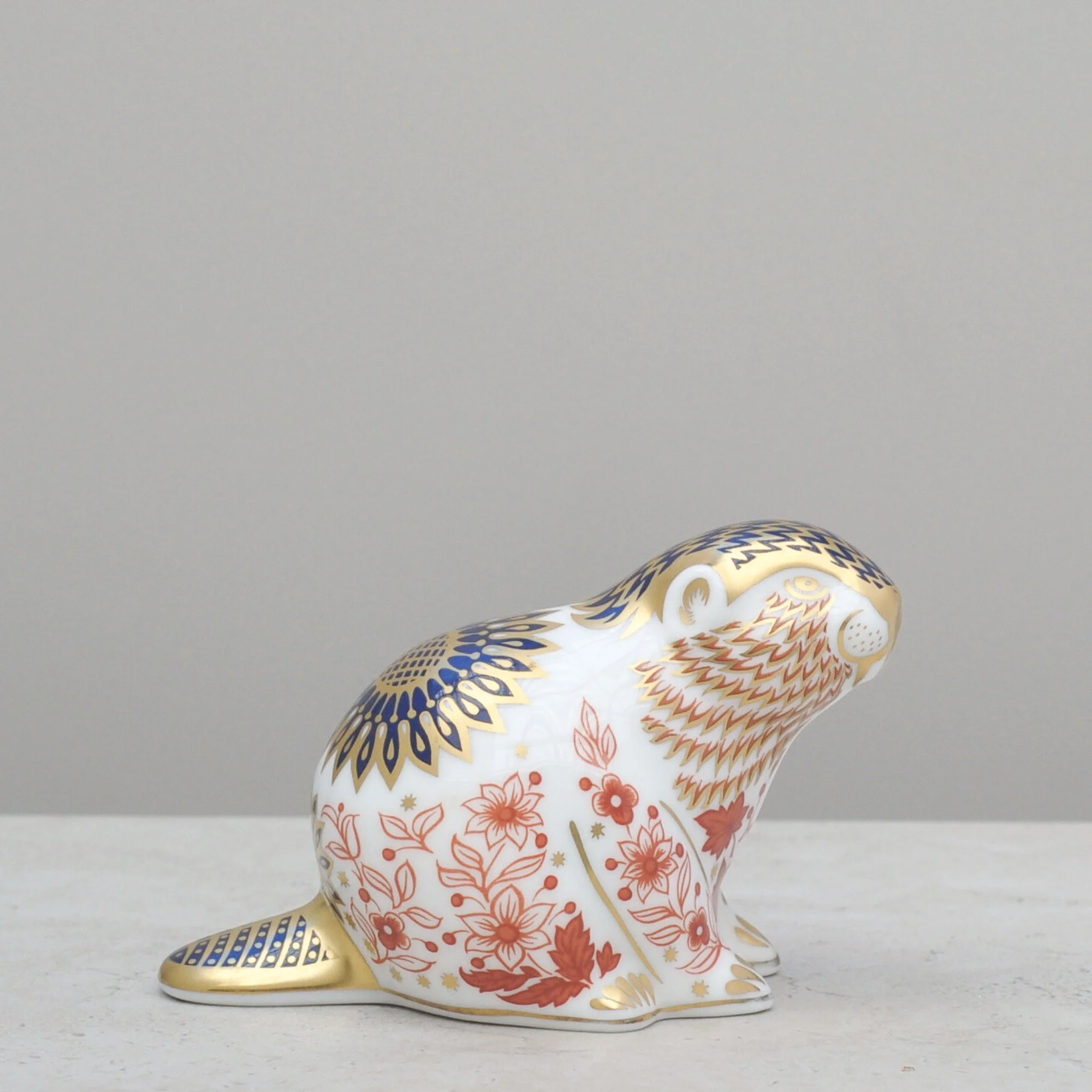 Left-side profile of a Royal Crown Derby beaver paperweight highlighting the detailed gold and blue crown motif.