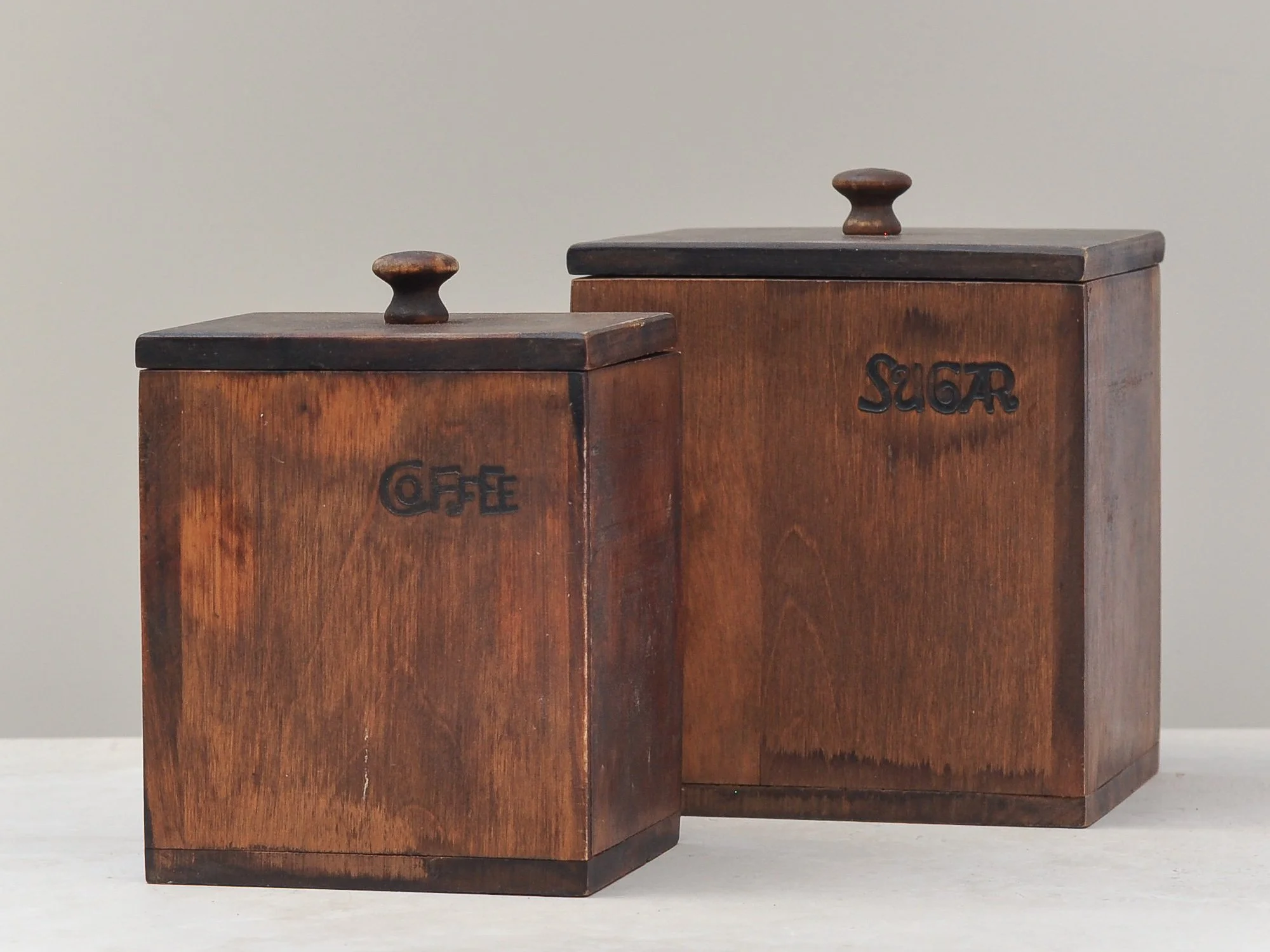 Close-up view of vintage wooden coffee and sugar canisters, showing carved labels and surface detail.