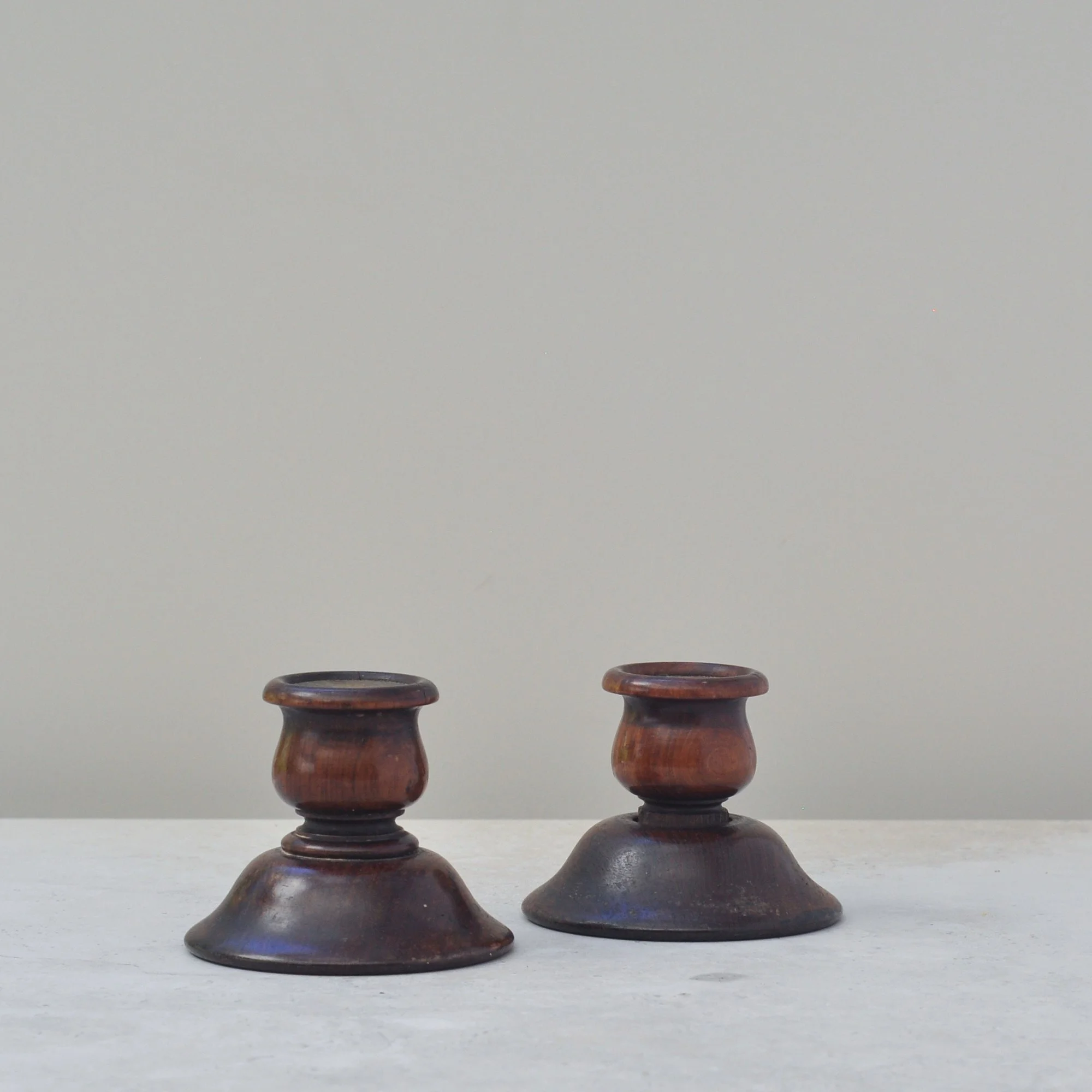 Pair of antique turned wood candlesticks with copper inlay, front view on grey-beige background.