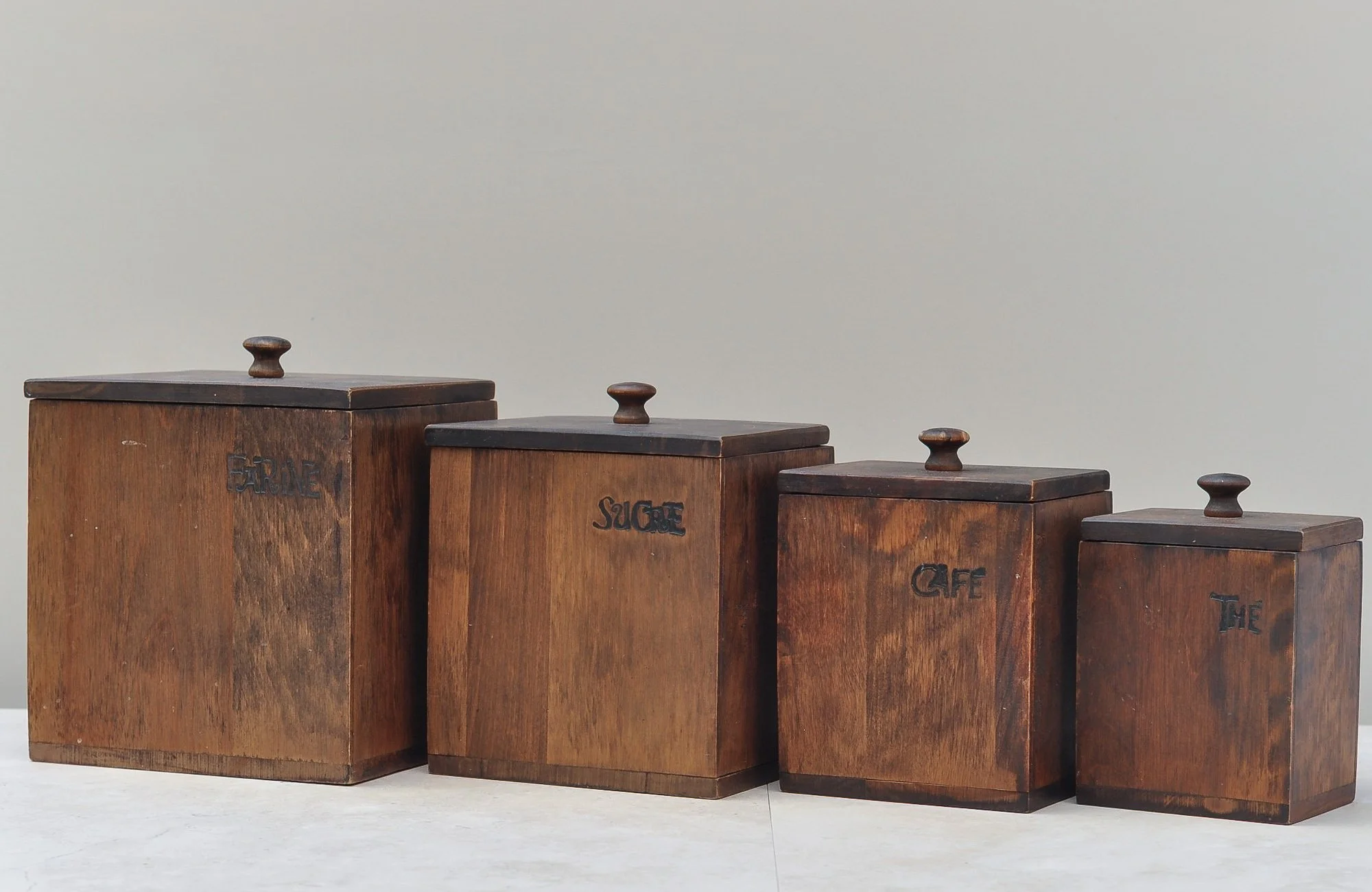 Vintage wooden kitchen canister set with carved labels, shown as a complete group with lids.