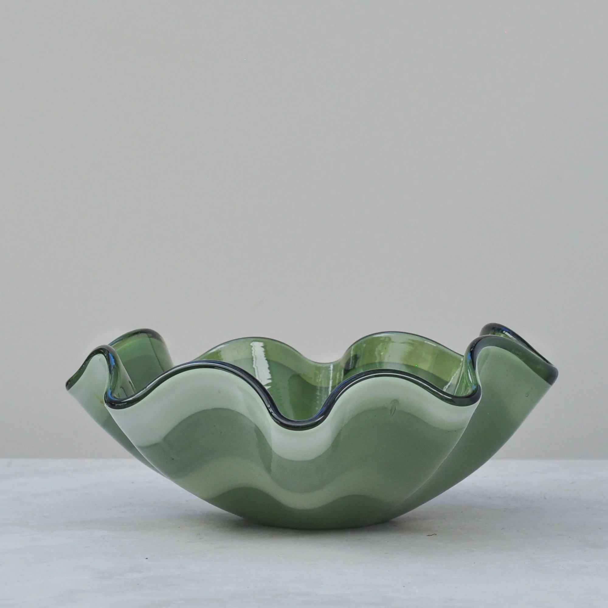 Olive green handblown glass bowl with wave edge and layered green tones.