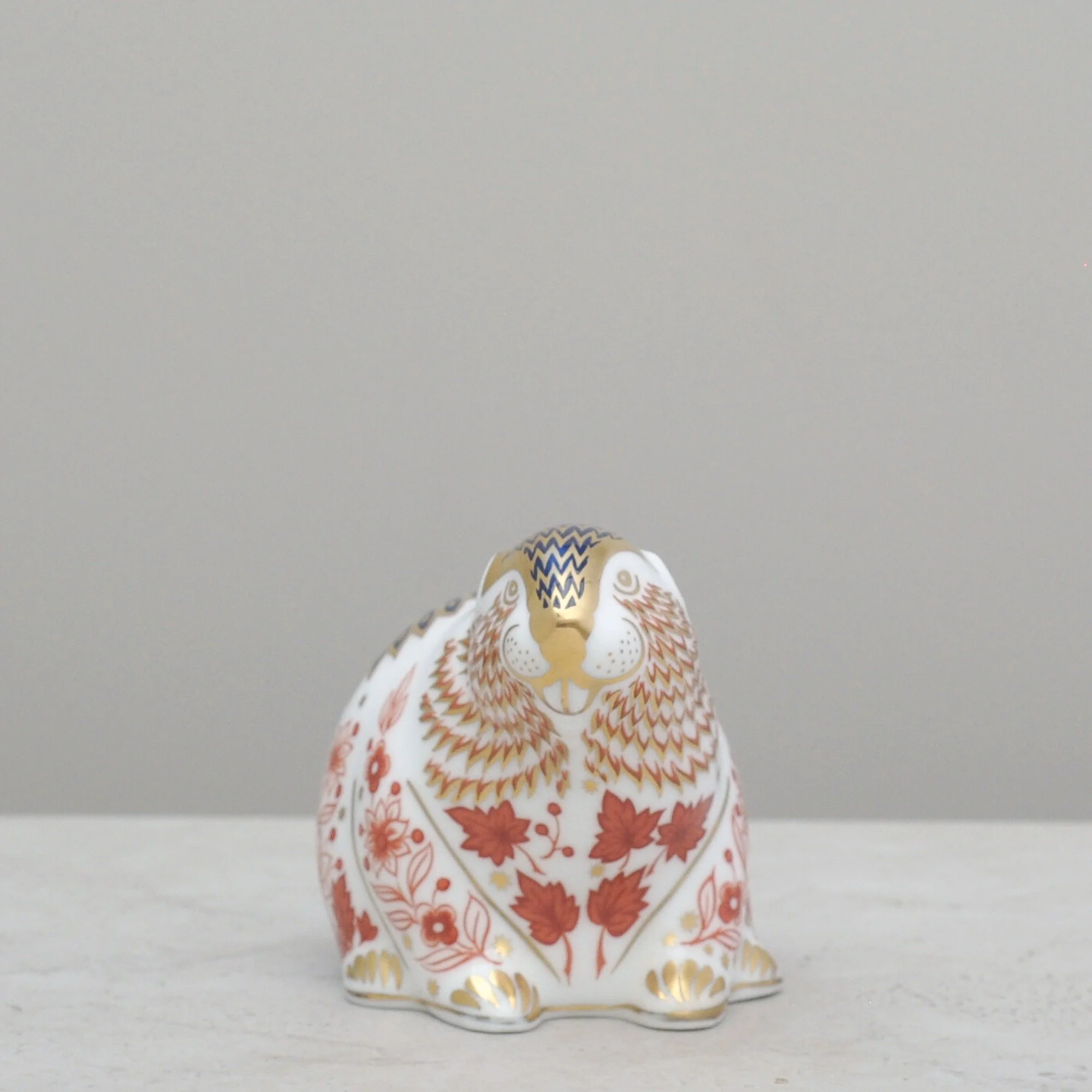 Front view of a Royal Crown Derby beaver paperweight with decorative floral and feather-style motifs in red, blue and gold.