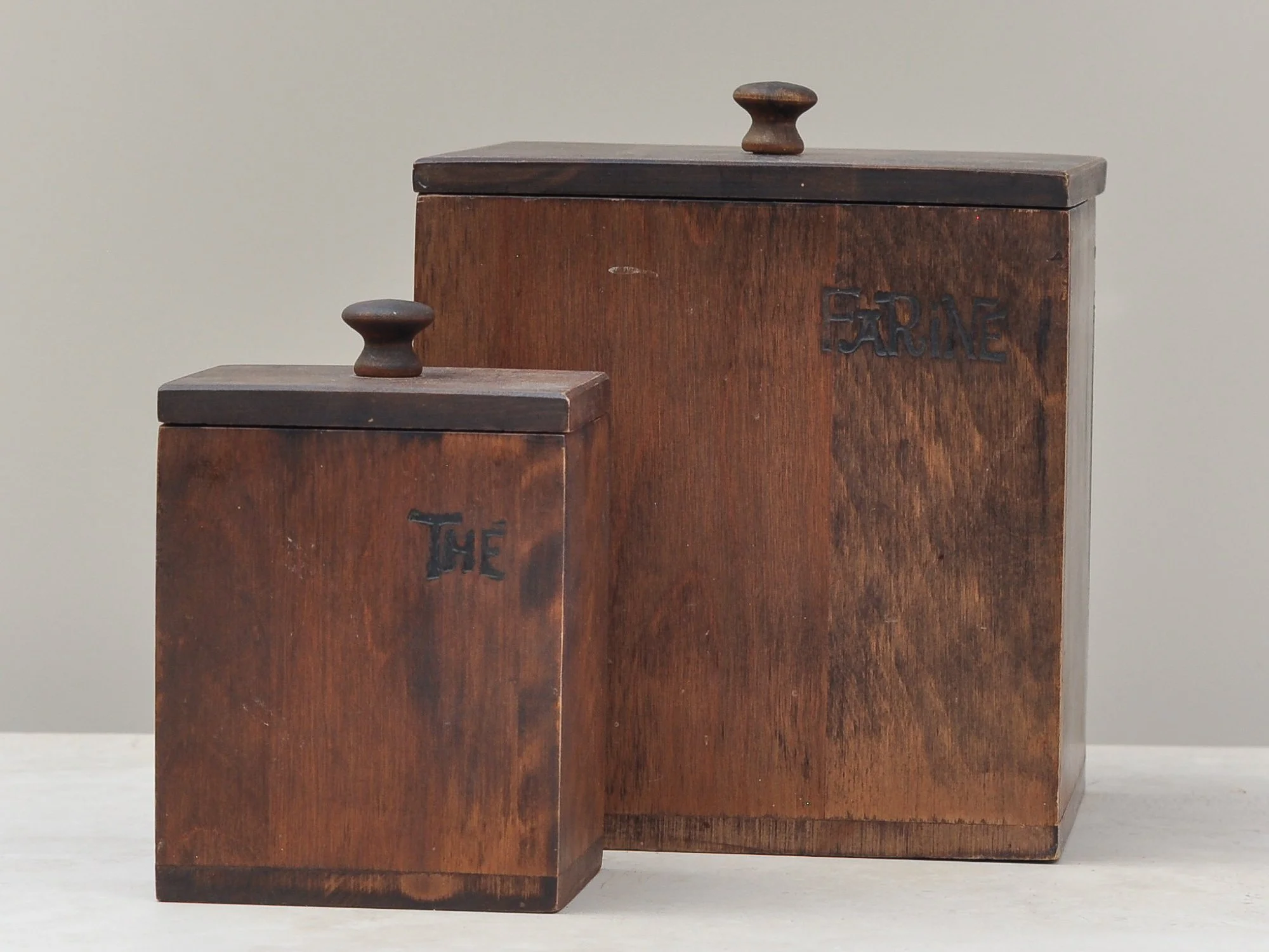 Pair of vintage wooden kitchen canisters with carved labels, shown together to highlight size contrast and patina.