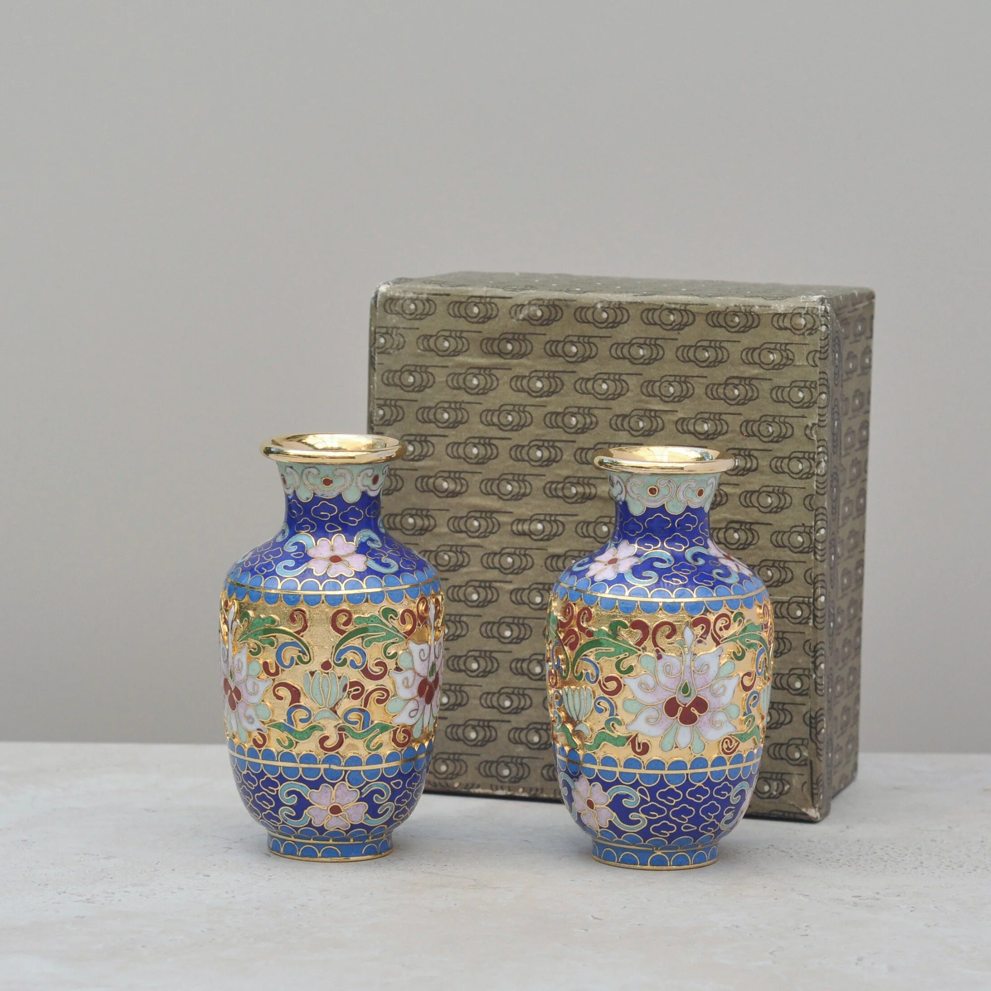 Cloisonné vase pair displayed alongside their original patterned storage box, highlighting condition and provenance.