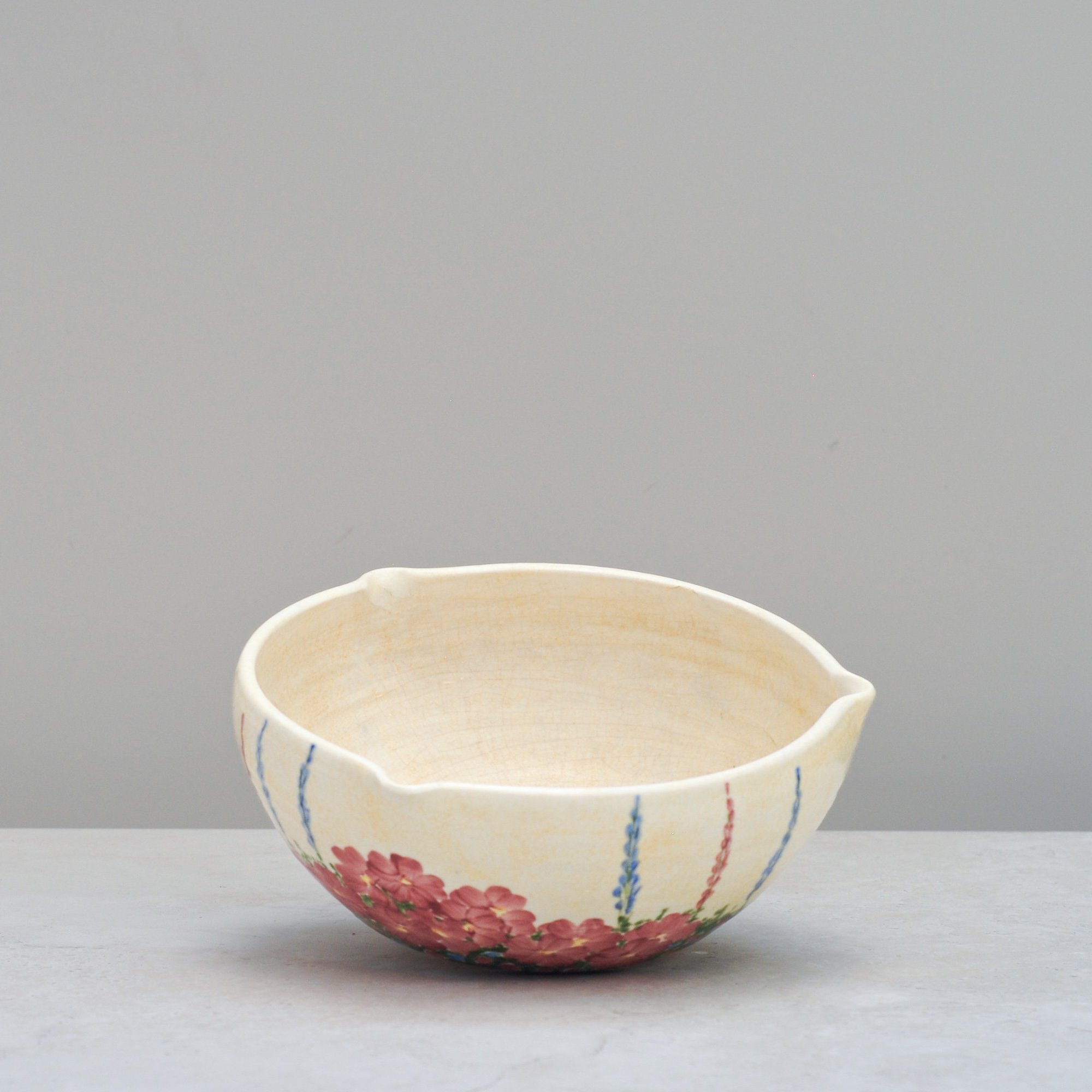 Art Deco E. Radford mixing bowl shown from an angled side view, highlighting its sculpted form and painted floral detail.