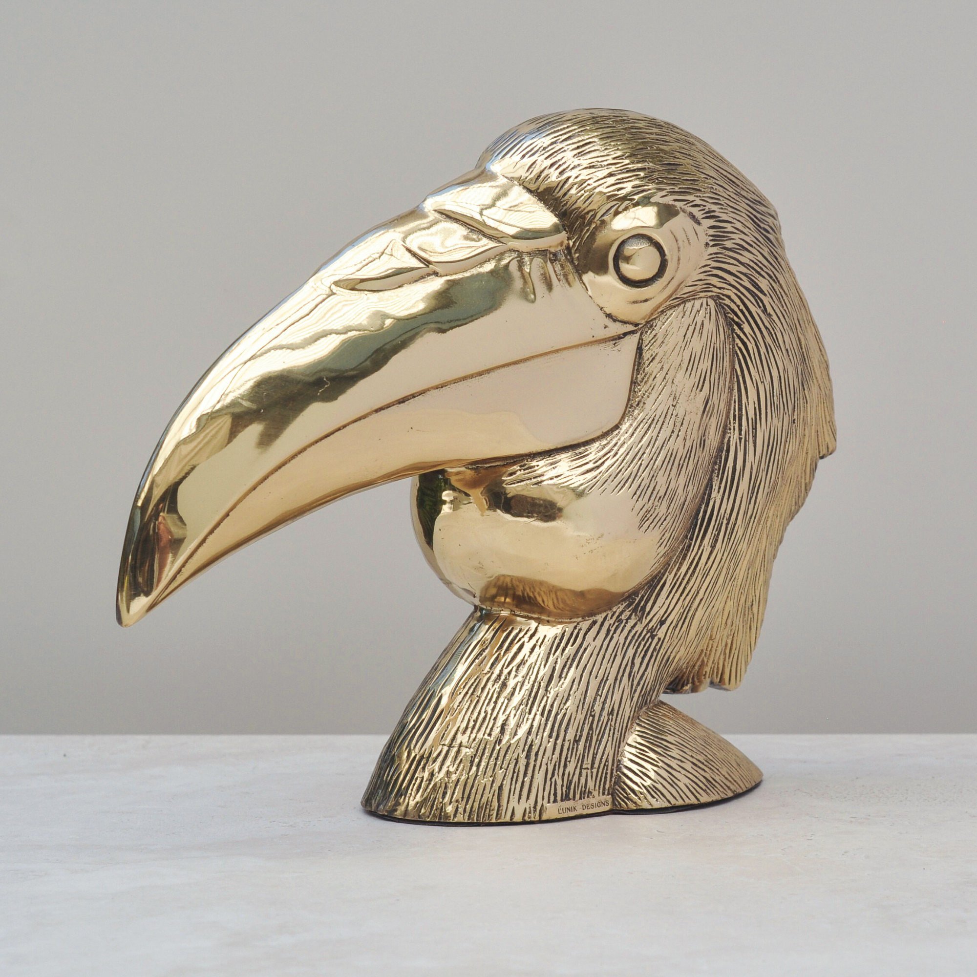 Side view of vintage brass bird head sculpture showing textured feather detail