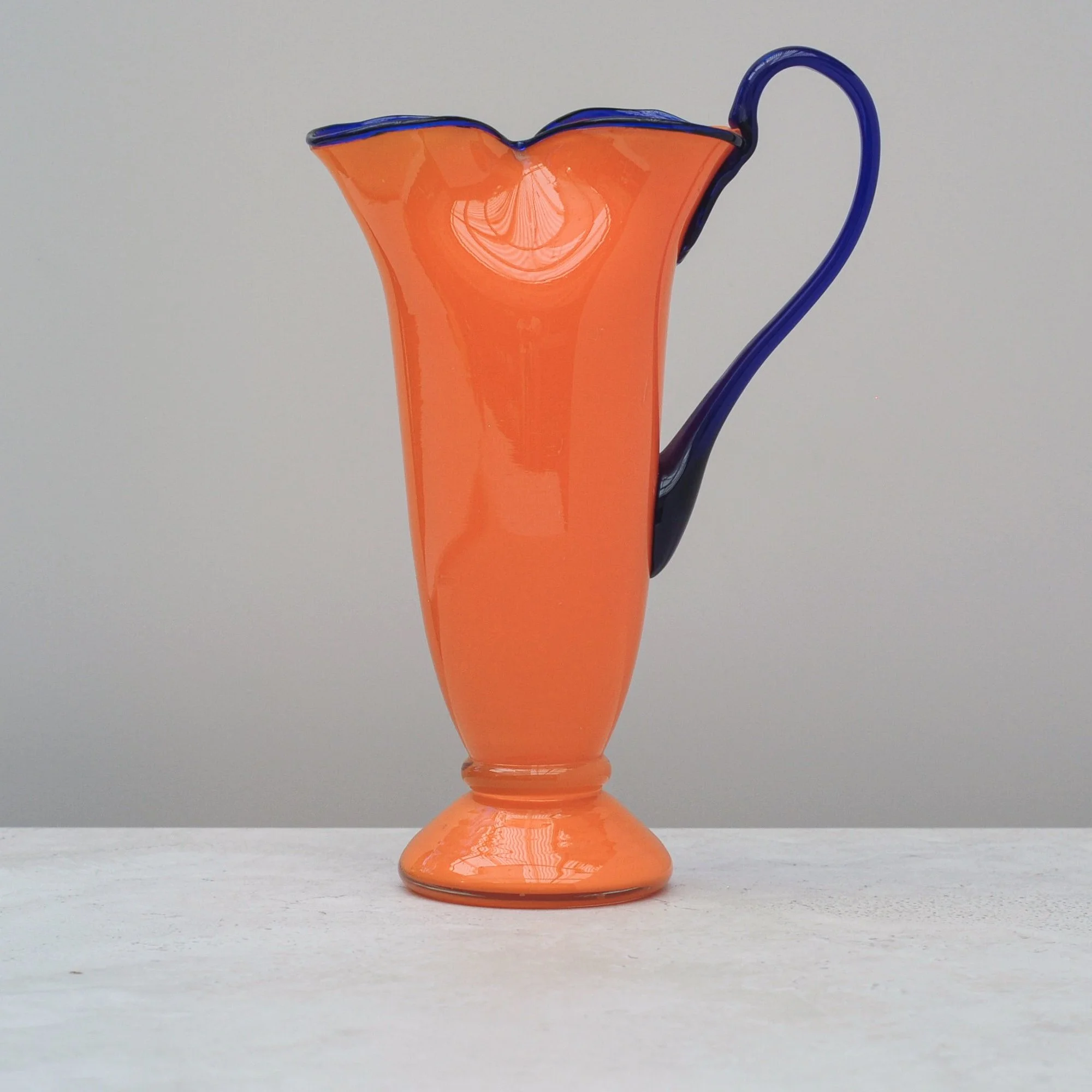 Art Deco Tango Glass jug in vibrant orange with cobalt blue rim and handle, front view