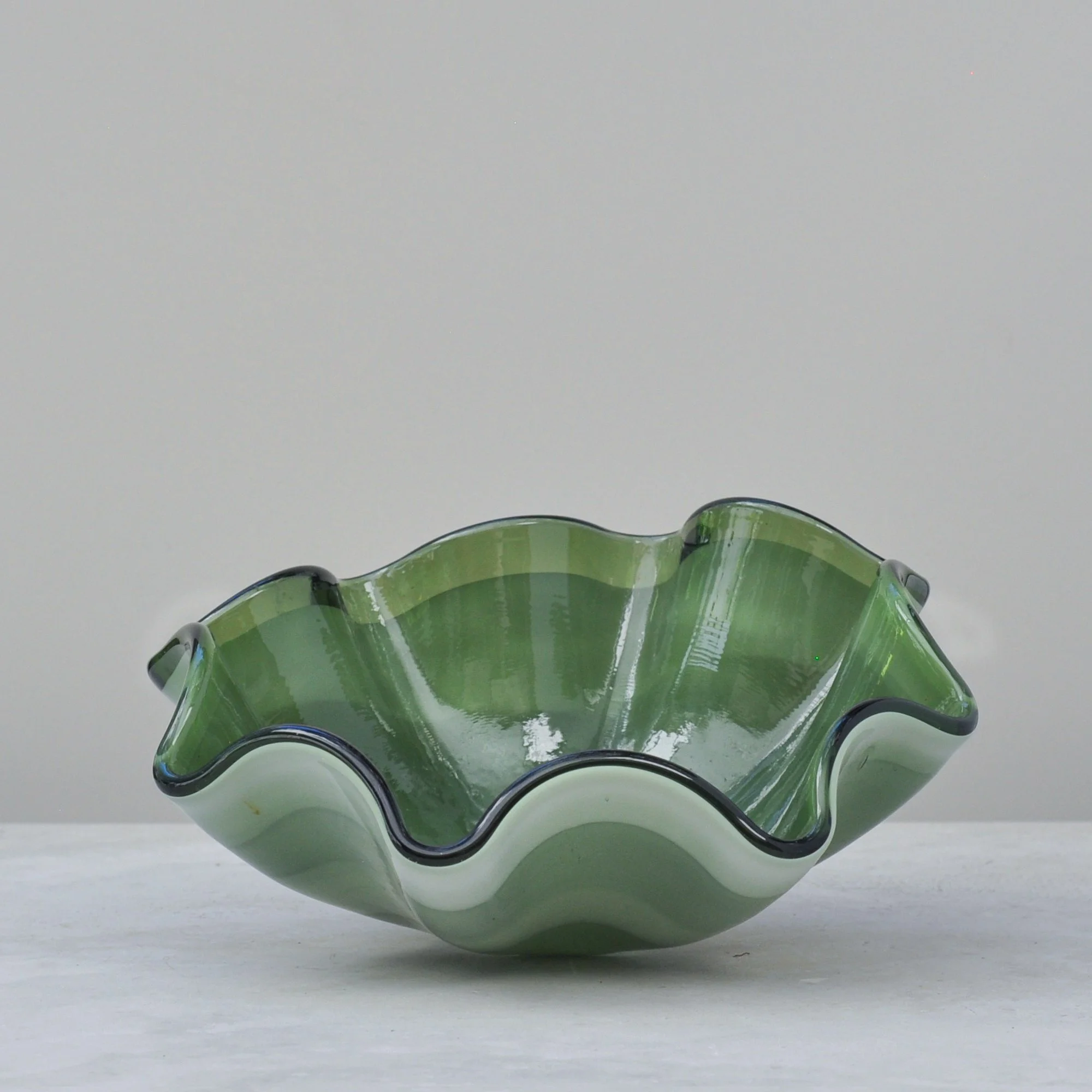 Side view of olive green wave-edge handblown art glass bowl.