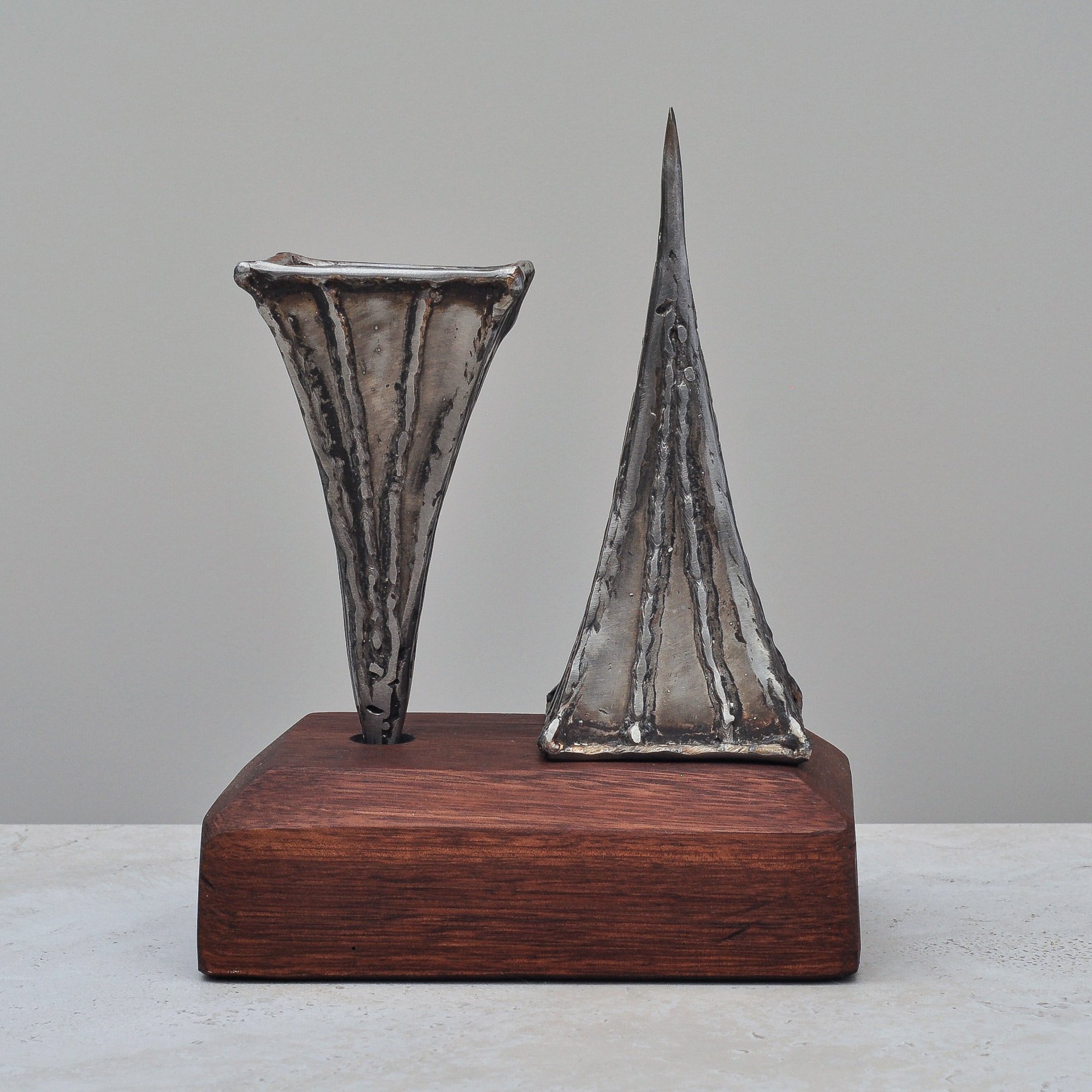 Three-piece arrangement showing two Brutalist metal vases and a tall sculptural metal form by Nik Markovina on a wooden base.