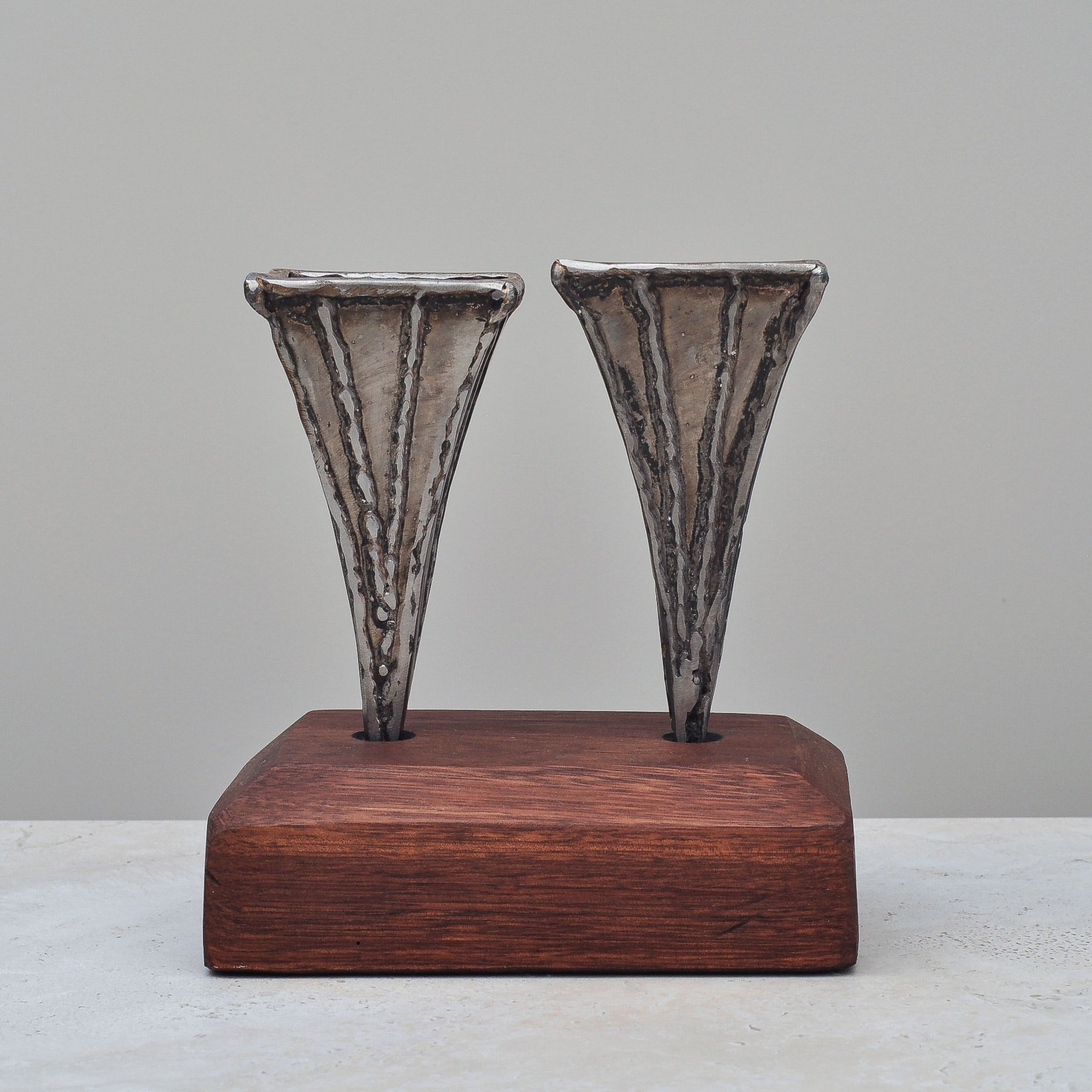 Front view of a signed pair of Brutalist metal vases by Nik Markovina (2003) displayed on a rectangular wooden base.