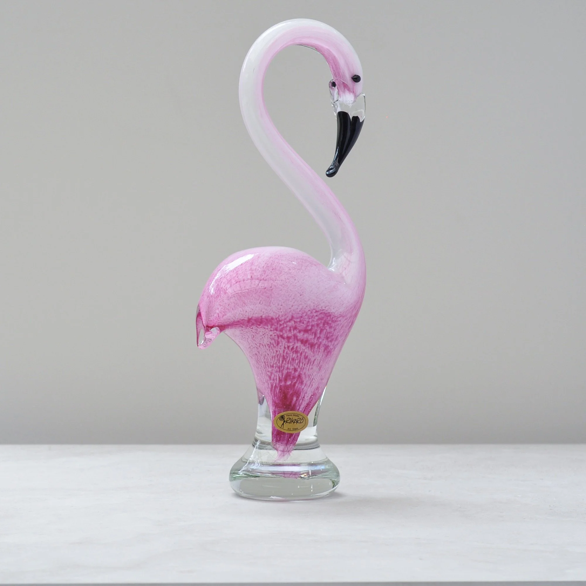 Hand blown glass flamingo sculpture in pink tones, front view on neutral background