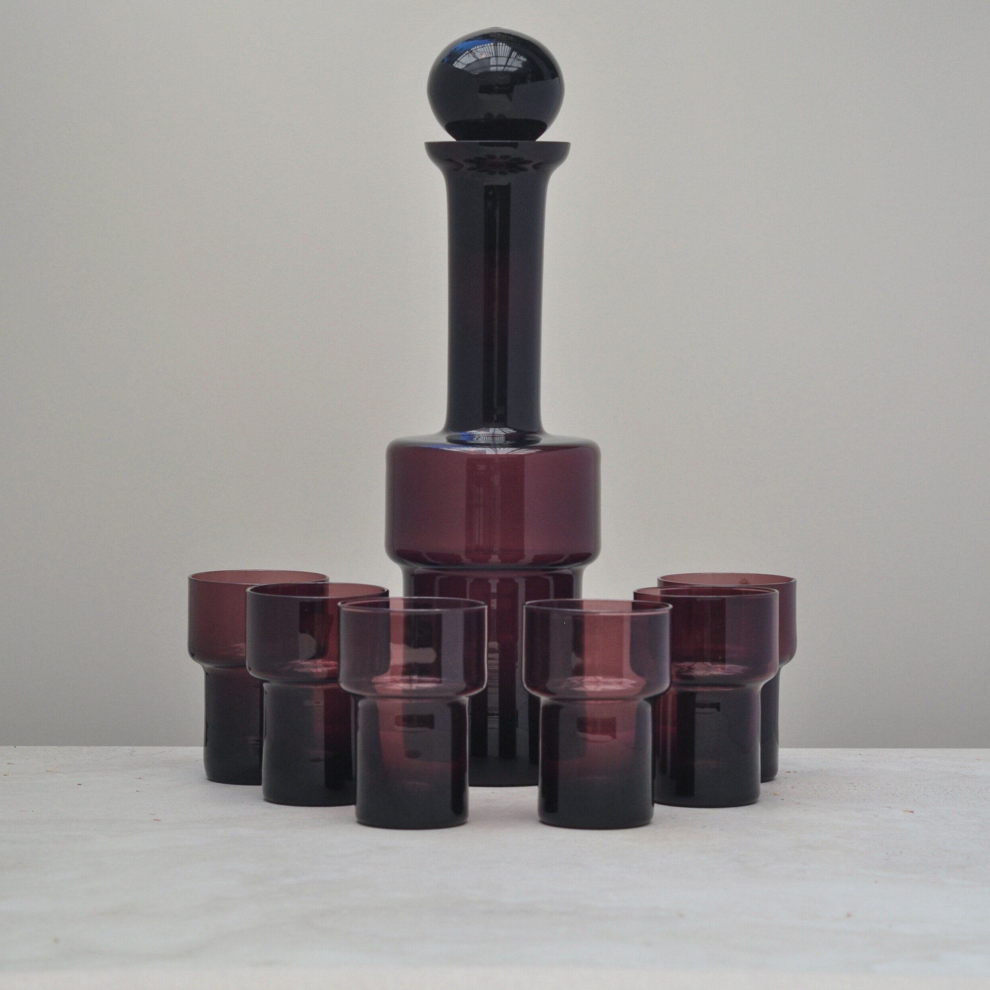 “Full set of vintage aubergine glassware featuring a tall decanter with stopper and six matching glasses arranged in a cluster.”
