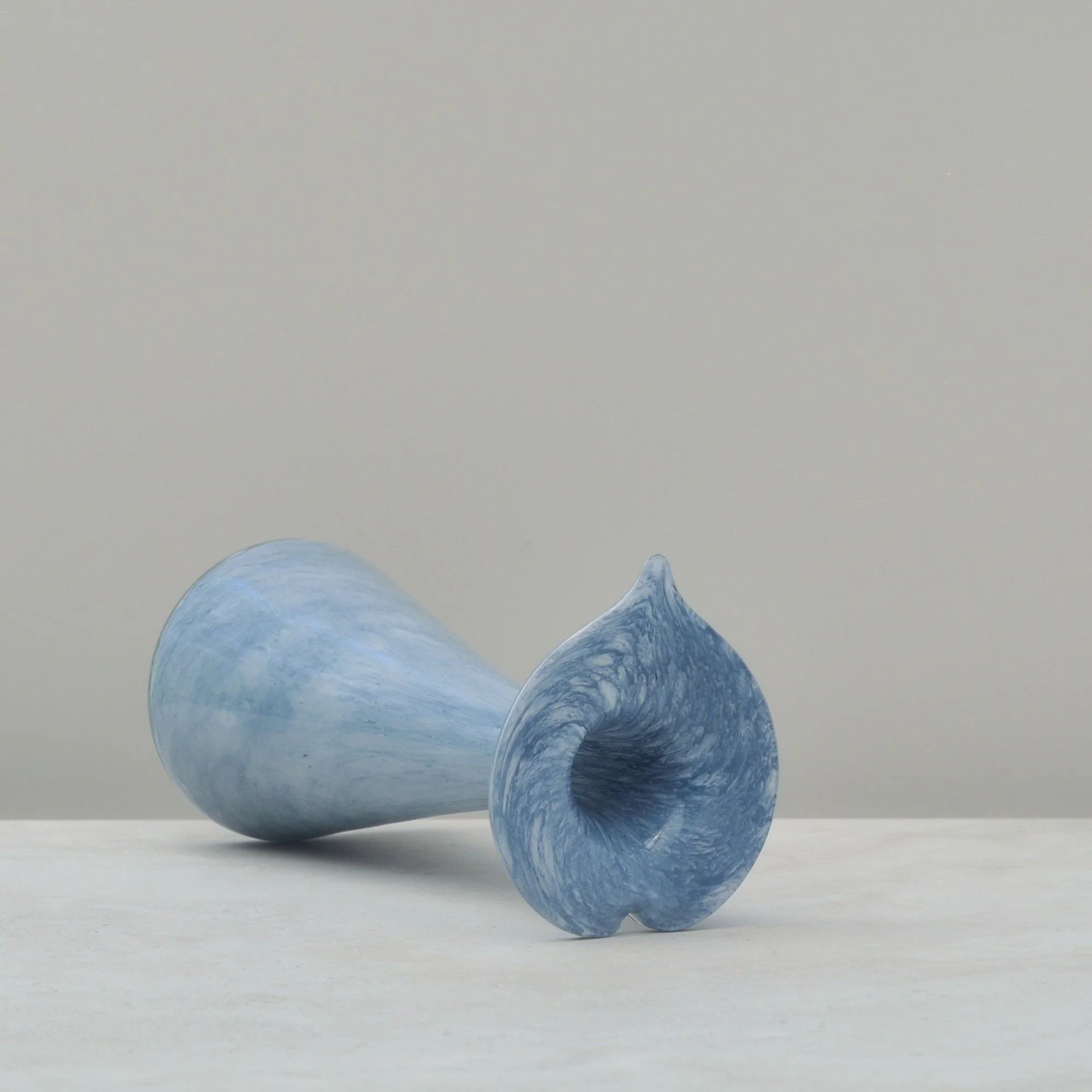 Light blue marbled glass vase lying on its side, highlighting the curved flared lip and handcrafted form.